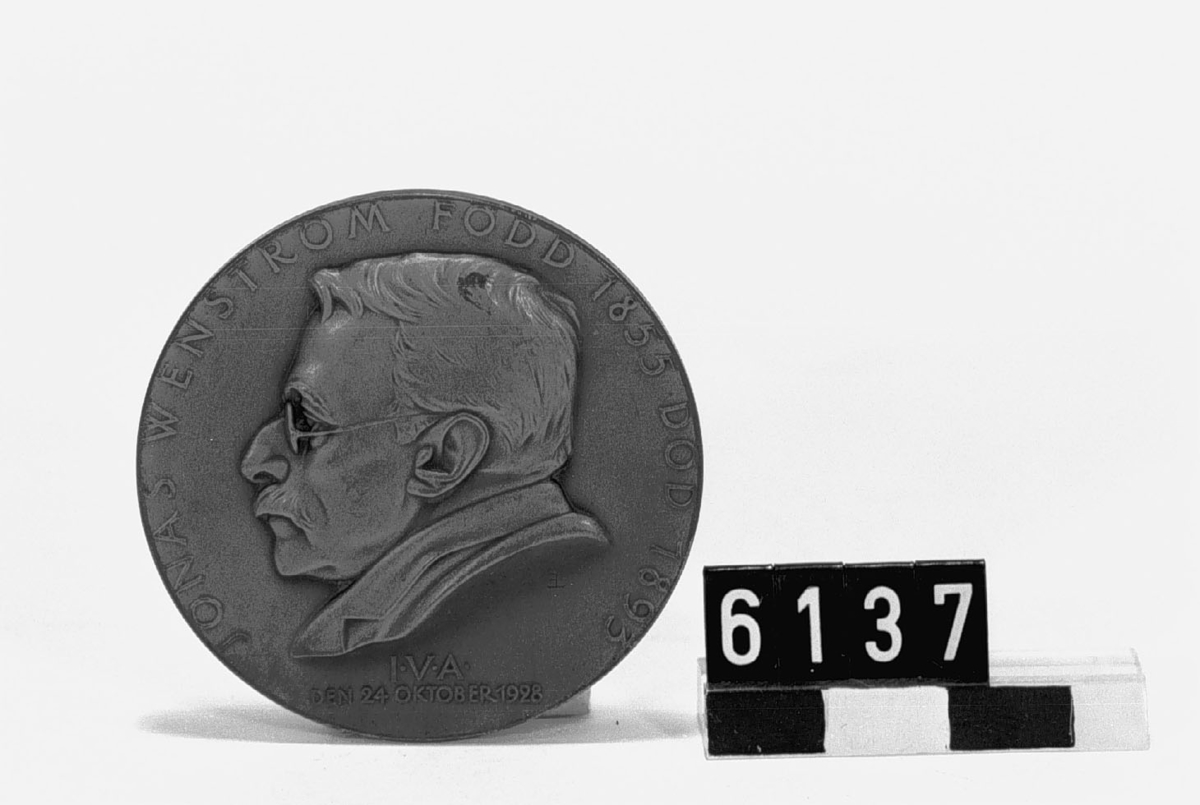 Medalj i brons över Jonas Wenström född 1855, död 1893. Tjocklek: 4 mm. Åtsidan: Porträtt i lågrelief vänster profil av J. Wenström och "JONAS WENSTRÖM FÖDD 1855 DÖD 1893". Text i nedre kanten: "I.V.A. DEN 24 OKTOBER 1928". Frånsidan: Prometheusfigur. Signerad: Erik Lindberg.