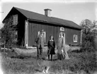 Familjegrupp tre personer och en katt.
Bostadshus i bakgrunden.