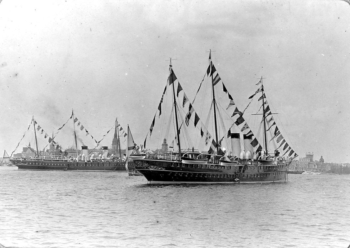 Fartyg, stadsvy med byggnader.
Stockholms ström med Gamla Stan i fonden. Ryska tsar Nikolaj II:s Stockholmsbesök 26-27 juni 1909, med de två kejsarjakterna Shtandart till vänster och Polyarnya Zvezda (Polstjärnan) närmast.