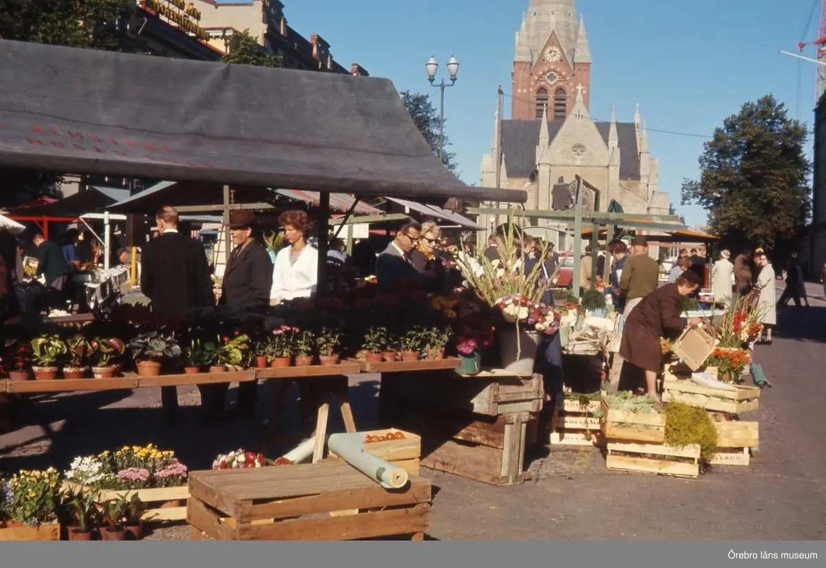 Stortorget med torghandel. 
Nikolaikyrkan i bakgrunden. 
Information från Trädgårdsmästare Börje Eriksson: det är Ove Almstedts torgstånd som ses på bilden. Det står snett på grund av att fjärrvärme håller på att grävas ner utanför Domus alternativ att Domusvaruhuset håller på att byggas. Bilden är tagen på 1960-talet.