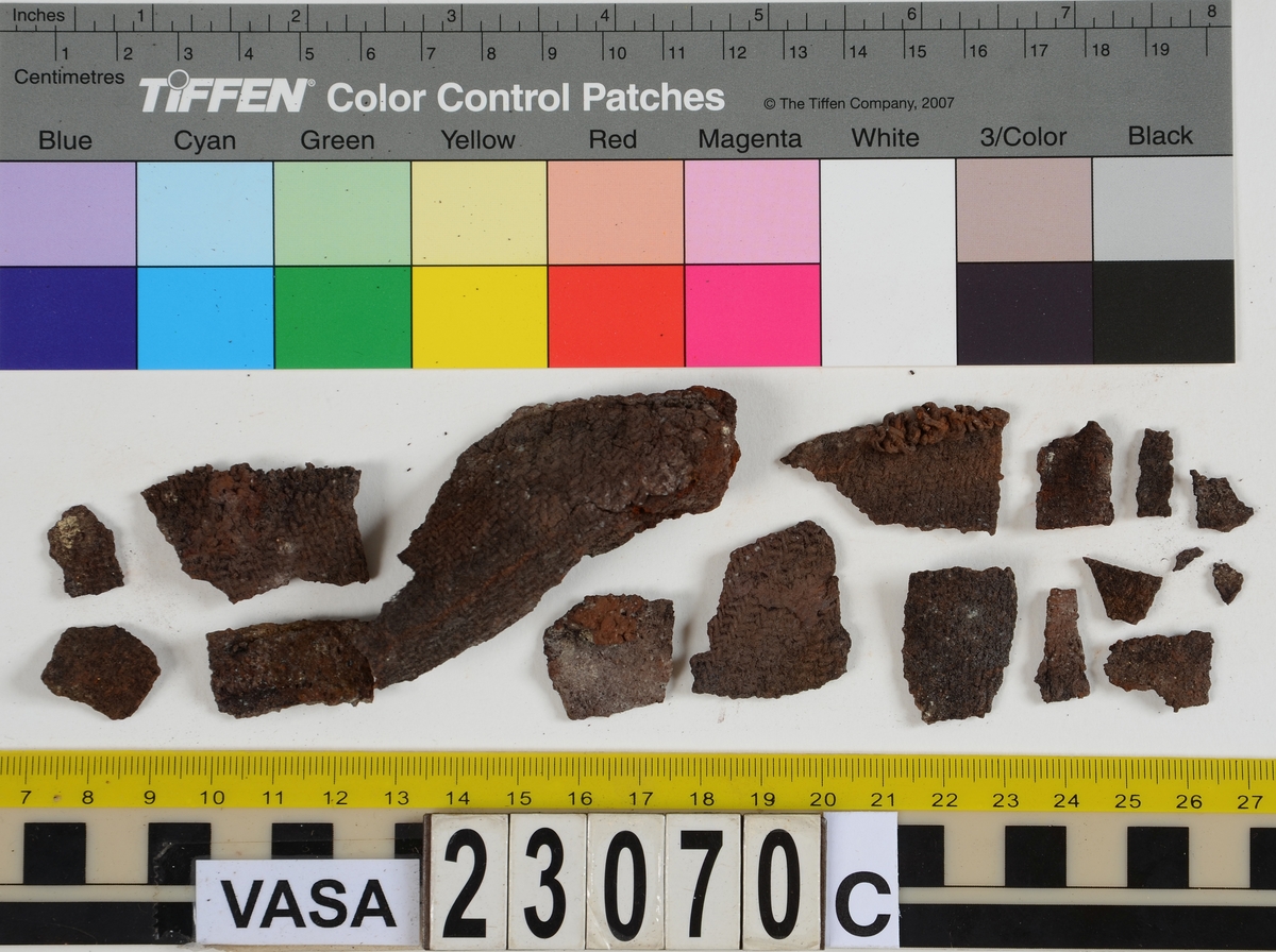 Sko.
Inuti skorna hittades även fragment från olika textilier som ursprungligen varit ett par strumpor. Idag sitter ett stickat fragment av ull fast i vänsterskon (23070) med avigsidan uppåt. I fyndet finns även en mängd lösa stickade fragment som idag är mycket korroderade och vissa helt mineraliserade av järn vilket har gjort textilen stenhård och därmed oerhört skör (23070a-c). Utifrån minskningar som några små fragment har så har det varit möjligt att rekonstruera strumpans tå. Genom att pussla ihop fragmenten som ursprungligen har suttit ihop har det på så vis gått att avgöra hur strumpans tå har varit konstruerad. Då textilen är så fragmentarisk är det inte möjligt att avgöra hur resten av strumpan har sett ut eller varit konstruerad. Däremot så finns det fragment av ett kypertvävt tyg av ull som på vissa ställen ligger dubbelt med det stickade 23070c). Ett av dessa fragment har stelnat i formen så som den suttit på fotens främre del inuti skon. Detta fragment täcker delvis det stickade tyget och har dessutom spår av kaststygn längs en kant. Så som det vävda tyget är placerat på det stickade tyget pekar på att man använt det som lagningslappar till sina stickade strumpor. 
I fyndet finns det även korroderade järnklumpar, ett tuskaftsvävt tyg av ull och rester av ett grovt bastfibergarn och två mindre läderfragment (23070d-f). Det är möjligt att även dessa har tillhört strumpan och/eller skon.

För mer detaljerad information från textildokumentationen (år 2022) se länkade filer.

Skodokumentation 2022:
Ovanläder. Tillverkad i getskinn av god kvalitet. Hör ihop med fyndnummer 23069 (Yngves skor). Tillverkades på en rak läst och bars på vänster fot. Inga dekorationer Det finns stygnhål som visar att det funnits invändiga förstärkningar (men förstärkningslappen saknas). Det finns delaminering men inga lagningar.
För mer information, se Länkade filer: Uppritning

Text in english:
This is the upper of a shoe of more “extreme fashion”, made of goatskin leather of good quality, probably made on a straight last and worn of the left foot, with no decorative features. The upper couples with 23069, together composing Yngve’s shoes. There are internal reinforcements missing from the upper and delamination, there are no repairs.
For more information, go to Länkade filer: Uppritning