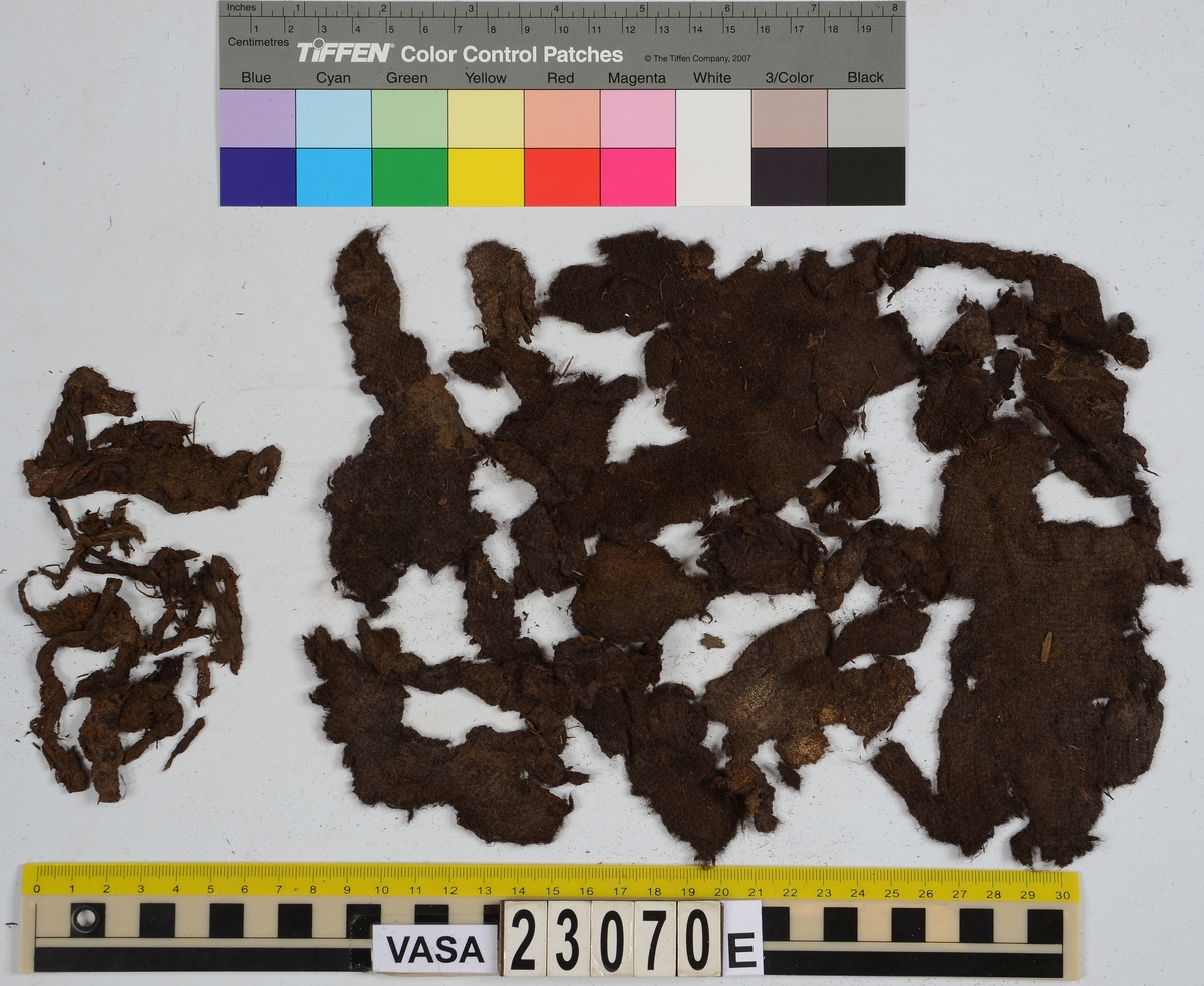 Sko.
Inuti skorna hittades även fragment från olika textilier som ursprungligen varit ett par strumpor. Idag sitter ett stickat fragment av ull fast i vänsterskon (23070) med avigsidan uppåt. I fyndet finns även en mängd lösa stickade fragment som idag är mycket korroderade och vissa helt mineraliserade av järn vilket har gjort textilen stenhård och därmed oerhört skör (23070a-c). Utifrån minskningar som några små fragment har så har det varit möjligt att rekonstruera strumpans tå. Genom att pussla ihop fragmenten som ursprungligen har suttit ihop har det på så vis gått att avgöra hur strumpans tå har varit konstruerad. Då textilen är så fragmentarisk är det inte möjligt att avgöra hur resten av strumpan har sett ut eller varit konstruerad. Däremot så finns det fragment av ett kypertvävt tyg av ull som på vissa ställen ligger dubbelt med det stickade 23070c). Ett av dessa fragment har stelnat i formen så som den suttit på fotens främre del inuti skon. Detta fragment täcker delvis det stickade tyget och har dessutom spår av kaststygn längs en kant. Så som det vävda tyget är placerat på det stickade tyget pekar på att man använt det som lagningslappar till sina stickade strumpor. 
I fyndet finns det även korroderade järnklumpar, ett tuskaftsvävt tyg av ull och rester av ett grovt bastfibergarn och två mindre läderfragment (23070d-f). Det är möjligt att även dessa har tillhört strumpan och/eller skon.

För mer detaljerad information från textildokumentationen (år 2022) se länkade filer.

Skodokumentation 2022:
Ovanläder. Tillverkad i getskinn av god kvalitet. Hör ihop med fyndnummer 23069 (Yngves skor). Tillverkades på en rak läst och bars på vänster fot. Inga dekorationer Det finns stygnhål som visar att det funnits invändiga förstärkningar (men förstärkningslappen saknas). Det finns delaminering men inga lagningar.
För mer information, se Länkade filer: Uppritning

Text in english:
This is the upper of a shoe of more “extreme fashion”, made of goatskin leather of good quality, probably made on a straight last and worn of the left foot, with no decorative features. The upper couples with 23069, together composing Yngve’s shoes. There are internal reinforcements missing from the upper and delamination, there are no repairs.
For more information, go to Länkade filer: Uppritning