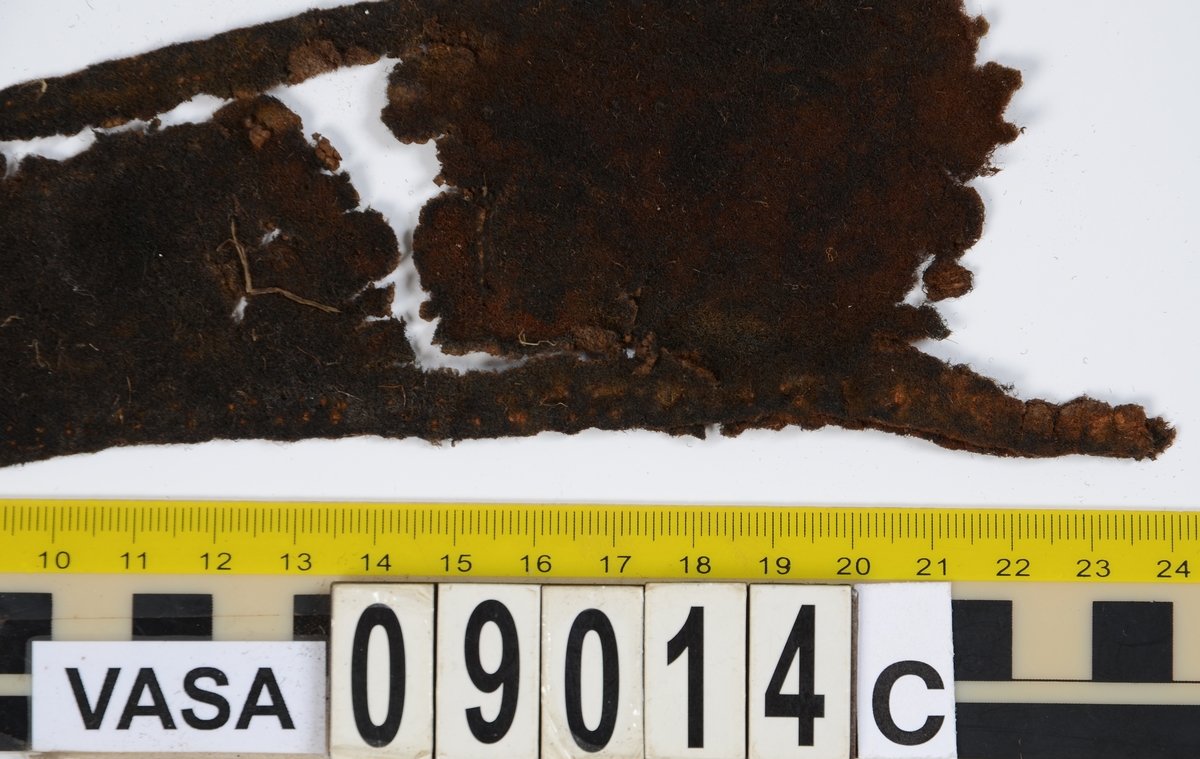 Textildokumentation 2018
Textil, fyndnumret består av mer än 50 st fragment uppdelade på 09014a-h.
Kontextgrupp ÖB20 (övriga fyndnummer i gruppen: 07732, 07762, 09228)
Relaterade fynd: Kontextgrupp ÖB17 och ÖB 18.
.
Fnr 09014a Typnr ÖB20.3:1
Sammanfattning - Ett textilfragment av ull vävt i tuskaft. Färgen är nu mörkbrun, fibrerna varierar i färg vilket tyder på att det är naturfärgad ull. Fibrerna är i vissa partier skadade på ytan och ser därför vita ut. Väven är tunn, jämn och fin och har inga spår av ytbehandling. Fragmentet har tre tillskurna kanter, två av dessa har spår av tre olika sömmar (söm 1: kvicksöm/förstygn). Formen tyder på att det är ett skört till en tröja. Andra delar: Jämför med 07726. 
.
Fnr 09014a Typnr ÖB20.4:1
Sammanfattning - Ett textilfragment av ull vävt i tuskaft. Färgen är nu mörkbrun, originalfärg okänd. I mikroskop ser tyget blåsvart ut. Väven är mycket jämn och slät. I sömsmånen på sida A finns bevarad lugg, på sida B är luggen så välbevarad att bindningen inte syns. Fragmentet har två tillskurna kanter med hål och avtryck av sömmar, även trådrester finns (söm 1: kaststygn - fälld kant, söm 2: ev förstygn - sammanfogande, söm 3: kaststygn - fälld kant). På sida B finns blåfärgad ull och silkesfibrer. 
.
Fnr 09014a Typnr ÖB20.5:1
Sammanfattning - Ett textilfragment av ull vävt i tuskaft. Väven är jämn och tät. En av kanterna är troligen tillskuren, inga sömrester finns. Tyget har inga spår av ytbehandling. På ytan finns en del bastfibrer. Relaterade fynd: Vävens struktur liknar ÖB20.4:1 men tygerna har ändå olika karaktär och detta fragment saknar lugg. 
.
Fnr 09014a Typnr ÖB20.6:1
Sammanfattning - Ett textilfragment av ull vävt i tuskaft. Färgen är nu brun, originalfärg är okänd men möjligen naturfärgad, fibrerna är mycket släta och varierar i färg från brun till nästan svart. Fragmentet är litet och mycket skadat, endast några få bindepunkter återstår vilket försvårar mätningar. 
.
Fnr 09014a Typnr ÖB20.7:1
Sammanfattning - Ett textilfragment av  ull vävt i tuskaft. Färgen är svartbrun, originalfärg okänd men möjligen naturfärgad då fibrernas färg varierar. Inga tydliga spår av ytbehandling. Väven är jämn men garnet är hårt spunnet vilket ger tyget en kypertkaraktär (falsk kypert). Fragmentet har inga tillskurna kanter eller sömmar. På ytan finns enstaka vita silkesfibrer.
.
Fnr 09014a Typnr ÖB20.8:1
Sammanfattning - Ett textilfragment av ull. Fragmentet är mycket litet och dåligt bevarat så bindningen är svår att avgöra, troligen 2/2 kypert. Färgen är svart, möjligen naturfärgad ull då fibrerna varierar något i färg. Tyget har ingen synlig ytbehandling. Garnet är hårt spunnet vilket ger tyget en speciell karaktär. 
.
Fnr 09014b Typnr ÖB17.1:8-11
Sammanfattning - Fyra textilfragment av ull vävt i tuskaft. Färgen är mörkbrun, originalfärg okänd men den bruna tonen slår mot röd. Tre av fragmenten har tillskurna kanter och spår av sömmar. Andra delar, som troligen kommer från samma tröja, är fnr 03261a och d, 09014h samt 09228a. 
Fragment ÖB17.1:9 - Fragmentet har två tillskurna kanter varav den ena har spår av en söm. Fragmentet är troligen sidostycket till en tröja. Den tillskurna kanten har då varit monterad mot tröjans bakstycke och bör ha hört samman med fyndnummer 03261d, vilket är ett bakstycke till en tröja.
Fragment ÖB17.1:10 - Fragmentet är mycket skadat men är troligen av typen ÖB17.1. Formen är densamma som för del av fragment ÖB17.1:9 och kan därför vara en dubblering av detsamma, alternativt det motstående sidostycket.
.
Fnr 09014c Typnr ÖB20.9:1-19
Sammanfattning - Nitton textilfragment av ull vävt i tuskaft. Färgen är brun, originalfärg okänd. Sida B har en kort tät lugg som döljer bindningen. På sida A finns ingen lugg och bindningen är synlig. Fjorton av fragmenten har tillskurna kanter och sömmar. Tre av fragmenten har sydda knapphål. Flera fragment är dräktdelar, till exempel finns en fragmentarisk krage. På ytan på flertalet fragment finns fibrer i flera klara färger, till exempel rosa, röd och blå. Vita fibrer finns i stor mängd, kan vara recenta.

Fragment ÖB20.9:1 - Fragmentet har flera tillskurna kanter med avtryck och hål efter olika typer av sömmar (söm 1: ev. sammanfogande, söm 2: kaststygn - fåll, söm 3: kaststygn - sammanfogande, söm 4: kaststygn - sammanfogande, söm 5: osäkert, söm 6: osäkert), trådrester finns. Kanterna och sömmarnas karaktär gör att sida A bedöms vara plaggets rätsida/utsida. Några hål som ej är stygnhål men kan vara original finns. I fragmentet sitter fast två stycken silkestrådar (söm 7: silkestråd med knut, fäst i tyget, söm 8:  silkestråd med ögla, fäst i tyget). Det är samma typ av tråd som knapphålen på fragment ÖB20.9:2 är sydda med. På sida A finns ett område med extra mycket korrosion och även en långsmal vitaktig avlagring.

Fragment ÖB20.9:2 - Fragmentet har inga bevarade tillskurna kanter, dock finns en någorlunda välbevarad rad med knapphål. Samtliga knapphål är trasiga i ena sidan så deras ursprungliga storlek går ej att avgöra. Knapphålen är sydda med knapphålsstygn i silkestråd och sitter med 13-15 mm mellanrum (c/c mått). Det tvärställda tränsen består av ca 10 stygn och syns ej på sida B, tränsens knutar sitter vända från knapphålet. På sida B anas rester av bastfiber under knapphålsstygnen, troligen från en dubblering av tyget eller ett foder. 

Fragment ÖB20.9:3 - Fragmentet har fyra stycken knapphål, varav ett är helt. Knapphålen är skurna på skrådden. Eventuellt finns spår av en söm längs en del av kanten. Knapphålsstygn och trådrester är mycket fragmentariska.

Fragment ÖB20.9:4 - Fragmentet har tre stycken knapphål.  Knapphålen är sydda med knapphålsstygn i silkestråd. Knapphålens längd är 19-20 mm och de sitter med 18-22 mm mellanrum (c/c mått). Eventuellt är fragmentets ena kant en sömsmån, kan ha varit monterad mellan andra tyglager (kanten har avvikande färg). Under knapphålsstygnen på sida B finns rester av annat material, eventuellt bastfiber. Bastfibrer finns också utspridda över ytan på sida B, kan vara rester av en dubblering till tyget eller ett foder, se fragment 9:2. På sida A finns avlagringar och korrosion. 

Fragment ÖB20.9:5 - Fragmentet har bristningar i tyget som ser ut som knapphål, dock finns inga rester av stygnhål eller tråd. Fragmentets ena kant är troligen en sömsmån, kan ha varit monterad mellan andra tyglager (kanten har avvikande färg). Enstaka spår av söm och tråd finns längs kanten (söm 1), dessa är mycket otydliga. På fragmentets andra (mycket trasiga) kant finns ett mycket tydligt stygnhål. Fragment 9:4 och 9:5 ser ut att kunna höra ihop, dock går trådsystemen åt olika håll så det är inte fallet.

Fragment 9:6-9 - Till det stora fragmentet 9:6 hör det lilla lösa fragmentet 9:7. I fragment 9:6 sitter två fragment fastsydda, 9:8 och 9:9. De sammansydda fragmenten har tre tillskurna kanter och spår av minst fem sömmar (söm 1: kaststygn, söm 2: förstygn el. liknande - sammanfogande, söm 3: kaststygn, söm 4: sammanfogande, fäster ihop 9:6 med 9:8 och 9:9, söm 5: två stygnhål), trådrester finns. Det är troligt att 9:8 och 9:9 är delar av samma tillskurna bit, och att den utgjort en dubblering till 9:6 (inklusive 9:7). Den tillskurna formen ser ut att vara en krage. Fragmentet skulle då vara en halv krage, bevarad från framkant till nästan mitt bak. På sida A finns en beläggning på delar av ytan. På sida B finns en mängd fibrer i klara färger: blå, vit, rosa, tegelröd, orange, karminröd, grön, mörkgul och grå. fibrerna ligger ytligt med nästan samtliga sitter delvis fast i tygets lugg eller har en eller båda ändar nere i vävens bindning. Fibrerna bör därför vara ursprungliga. Sida A har en mindre mängd av nämnda fibrer, mest förekommande på ytan av fragment 9:8 och 9:9.

Fragment ÖB20.9:10 - Fragmentet har två tillskurna kanter. Dessa är invikta mot sida B som en 6-7 mm bred fåll som är fastsydd med kaststygn, trådrester finns (söm 1 och 2). Fragmentet kan vara ett skört till en tröja. På båda sidors yta finns fibrer i klara färger: grå, ljusblå, orange, orangebrun, vitgul, blå svart, vit, röd, korallröd och rosa.

Fragment ÖB20.9:11 - Fragmentet har tre tillskurna kanter med sömmar. Två av kanterna är invikta och fastsydda mot sida B, som fållar (söm1: kaststygn - fåll, söm 2: kaststygn - fåll). Stygnen går ej igenom till sida A men sömmen syns som bucklor i fragmentets yta. Söm 3 längs den tredje kanten har troligen varit en sammanfogande söm sydd med kaststygn. Stygn och trådrester finns bevarade från samtliga sömmar. Under fållen vid söm 1 finns ett litet fragment av en annan textiltyp. Troligen ursprungligen en dubblering eller liknande. Fragmentet är ca 10x5 mm stort och har fått typnummer ÖB20.16:1. På ytan på sida B finns enstaka bastfibrer.

Fragment ÖB20.9:12 - Fragmentet har två tillskurna kanter med sömmar (söm 1: ev kaststygn, söm 2: osäker). Vid söm 2 är sömsmånen vikt mot sida B. Vid söm 1 är kanten inte vikt. Fragmentet har samma form som ÖB20.9:6, "kragen".

Fragment ÖB20.9:13 - Fragmentet har två tillskurna kanter med sömmar (söm1: sammanfogande, söm 2: osäkert). De två övriga kanterna är eventuellt också de tillskurna men spår av eventuella sömmar är för otydliga. Enstaka fibrer med klara färger (rosa, blå, vit) finns på båda sidor, fler på sida B. Vid söm 2 finns på ett ställe en fiberknippa som kommer upp ur vävens bindning, kan vara rester av en tråd och är eventuellt halsplat silke. 

Fragment ÖB20.9:14 - Fragmentet har en tillskuren kant med söm (söm1: ev sammanfogande). I stygnhålen finns rester av tråd.
.
Fnr 09014c Typnr ÖB20.10:1
Sammanfattning - Ett textilfragment av ull vävt i tuskaft. Färgen är brun, originalfärg okänd. Sida B har en kort och tät lugg, bindningen syns bara på sida A. Längs ena kanten finns tre stycken tydliga hål. Hålen är gjorda med ett verktyg som skär av fibrerna snarare än tränger undan dem.
.
Fnr 09014c Typnr ÖB20.16:1
Sammanfattning - Fragmentet är mycket litet och sitter inuti den invikta fållen på fragment 09014c ÖB20.9:11, det sticker bara fram någon millimeter. Fragmentet är mycket skört. Bevarandegrad och storlek gör mätningar svåra. Det är olika garn i trs 1 och trs 2. Sida B är täckt av en lugg, på sida A syns bindningen, om än fragmentariskt.
.
Fnr 09014d Typnr ÖB18.16:2-8
Ej dokumenterad
.
Fnr 09014d Typnr ÖB20.11:1-2
Ej dokumenterad
.
Fnr 09014e Typnr ÖB20.12:1-4
Sammanfattning - Fyra textilfragment av ull vävt i tuskaft. Färgen är brun med inslag av täckhårsfibrer i en mörkare brun färg, originalfärg okänd. Fragmenten är mycket fragmentariska med trs 1 bättre bevarat än trs 2. Enbart på en del av fragment ÖB20.12:1 finns trs 2 samt bindningen bevarad. Utspridda över tygets yta finns grova bastfibrer samt korrosionsfläckar. 
.
Fnr 09014f Typnr ÖB20.13:1
Sammanfattning - Ett textilfragment av ull vävt tuskaft. Färgen är mörkbrun, fibrerna varierar mellan ljus och mörk brun. Originalfärg okänd, möjligen naturfärgad ull. Garnet är hårt spunnet vilket ger väven en särskild karaktär, sida A har en mer strukturerad ytan än sida B. Fragmentet har inga tillskurna kanter. På sida A finns enstaka röda och gulgröna silkesfibrer, samt bastfibrer. På sida B finns enstaka blå, vita och rosa silkesfibrer.
.
Fnr 09014g Typnr ÖB20.14:1-3
Sammanfattning - Tre textilfragment av ull och bastfiber vävt i tuskaft. Färgen är beige för bastfibern (trs 1) och svartblå för ullen (trs 2). Trs 2 är mycker grövre än trs 1. Trs 1 är nästan helt försvunnet. Två av fragmenten har tillskurna kanter och ett har spår av en sömsmån. På ytan av fragmenten finns en stor mängd bastfiber samt en vit/rosa tuss med silke. På fragment 14:2 finns några intensivt blå ullfibrer.
.
Fnr 09014h Typnr ÖB17.1:12-13
Sammanfattning - Två textilfragment av ull vävt i tuskaft. Färgen är brun, originalfärg okänd. Det större fragmentet är tillskuret och har spår av sömmar. Fragmentet är en ensömsärm med sömmen placerad mitt bak på ärmen. På ytan finns stora rostfläckar. Andra delar: Hör troligen (trots färgskillnad) till skelettet Beatas tröja, se fnr 03261a-d, 09228a, 09014b och h.