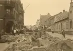 Algatan-Kontinentgatan mot väster, gatuarbete , till vänster. Krenziskys hus? Bankahörnan,  gruppbild,till höger Smiths handelsgård,  John Rasmussons jernhandel.