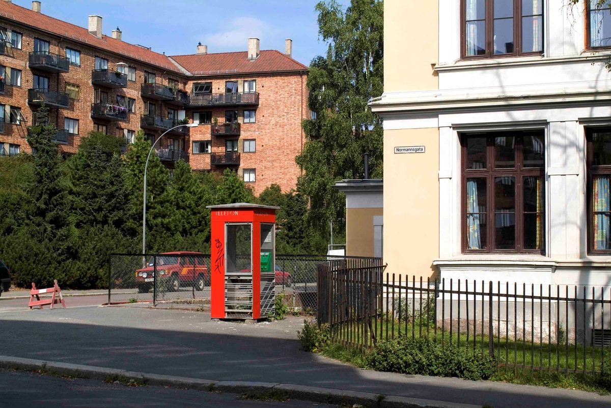 This is the story of how Norway’s most important conversation-space was designed by a young, freshly graduated man from Bergen.

“Norwegian architects are hereby invited…”
In the autumn of 1932, Oslo Telefonanlegginitiated an architectural competition. Finally, Oslo would get its own telephone booth. The city had had so called “talking-stations” from 1885, which in turn were overtaken by automatic telephones 
 only available at selected Narvesen kiosks. The state 
was of the opinion that now was the time to offer the public a better service; public telephone booths open 24/7, like the ones they already had in Sweden and England. But what would they look like, these new telephone booths? What considerations would it
 be necessary to take when designing it? The telegraph board developed a detailed list of demands and restraints: “The booth is intended to be placed outside on the streets and squares and need to be designed so that snow and ice does not hinder the opening and closing of the doors,” they wrote. “To prevent vandalism, theft, uncleanliness etc. inside the booth, it needs to be designed so that from all angles one may see what is going on in there.” Additionally, it would need to withstand storms and bad weather, and “preferably also being whipped by rain mixed with seawater” 

This was not all: The appearance would have to be «pleasing». The booth also needed to be movable, so that it could be taken in to be serviced at Telegrafverket’s main workshops. The reqired material was iron, and the surface was to be spray painted  preferably using car-body paint. There was a requirement for “a writing shelf, a pack shelf, and a suitable place for the telephone catalogue.” Also, there would need to be an illuminated TELEFON  sign, easily visible from all four angles. The total cost for each booth should not exceed 1000 kroner. The first prize for coming up with such a product was 800 kroner.

“Norwegianarchitects are hereby invited to partake in a competition for the design of a telephone booth…”  

The man with the solution
«At some point in 1932, Georg Fredrik sat at a party in Bergen. Maybe he felt a bit lost and forgotten as he often had throughout his life. He retreated to a quiet corner, took out a pencil and strted doodling on a matchbox.  According to my mother, this was how the telephone booth came into being.” In the book “Norges lille røde  historien om telefonkiosken,” Lars Fasting describes his father, the man who is far less known than the iconic architctural structure he left behind. Georg Fredrik Fasting was from Bergen, born into a family of working people and smallholders. One unusual facet of Georg Fredrik was that he was born without ears. His mother made sure he learnt to speak, read and write, 
ut Lars Fasting indicates that his father would seek refuge in drawing when the social challenges became too much to bear. And in the end drawing became his profession. In 1924 he secured a guarantor for a student loan, and started studying to become an a
rchitect at the NTH. Throughout the 1930s he entered several architectural competitions, with drafts produced, according to his son, “after work and in the late hours of the night.”

His efforts were not wasted. Out of 93 entries, with names such as “Flirt”, “Brrr”, “Ring” and “Amor”, the jury selected Fasting’s submission, “RIKS” as the new telephone booth: “The draft shows a strikingly simple solution to the task, technically as well as aesthetically well worked out.”

Taut and provident
Simple and aesthetc are the keywords here. Fasting had designed a booth pointing towards the future, and to modernism. Just how modern it was can be seen by comparing RIKS to the British telephone booth, also designed in the interwar-era. While the British version with it classicistic style is looking back to the heyday of the empire, Fasting’s booth is progressive and functionalistic. Like most Norwegian architects, Fasting broke with the classicistic style of architecture after the Stockholm-exhibition in 1930. “After it, almost all buildings erected in Norway until the German invasion in 1940, were in the functionalistic architectural style,” writes senior curator of architecture at the Norwegian National Museum, Ulf Grønvold, in the book, “Den lille røde”.“TheNorwegian booth is a piece of functionalistic architecture, an asymmetric composition with its roof slab overhanging the word TELEFON, in bold sans seraph lettering,”concludes Ulf Grønvold.

Fashionably red
And it was red. Fasting chose a colour which was part of the modern palette. “A bright red colour, but not as shiny as a signal red, the character of the colour places it among the fashionable colours within functionalism,” states paintings conservator and researcher in NIKU (Norwegian Institute for Cultural Heitage Research), Jon Brænne. In his opinion, Fasting went for visibility without making the booth stand out too much from its surroundings. The original colour was in use up to around 1950, when it changed to signal red. Towards the end of the 1970s the clour was again adjusted towards today’s orangey red.

The design, however, has not changed. RIKS is eighty years and still looks remarkably good. That’s what makes Fasting’s telephone booth a classic  even before it was added to DOCOMOMO’s list over moden icons of design. For Telenor, the telephone booth has served as a pathway into the hearts of the public. For many, Telenor (Televerket) was synonymous with exactly this telephone booth, because this was where one would go to place a call. Having a home
phone was not common until the 1980s. As such the red box became part of the Norwegian everyday and consciousness. The symbol- and publicity value of this is hard to evaluate, but in 2007 it was time to give honour where honour was due, Telenor, in consul
tation with the Directorate for Cultural Heritage, decided to preserve 100 telephone booths for all eternity.

And what about Georg Fredrik Fasting? What happened to him? At the age of 56 an entry in his diary states: «I CAN HEAR». As the first person in th world he had undergone an operation where he had ear canals constructed and eardrums fitted. For the rest of his life, the man behind Norway’s own telephone booth could answer the telephone himself.

Source: Norges lille røde historien om telefonkiosken (2007), issued by The Norwegian Telecom Museum and Telenor Cultural Heritage.