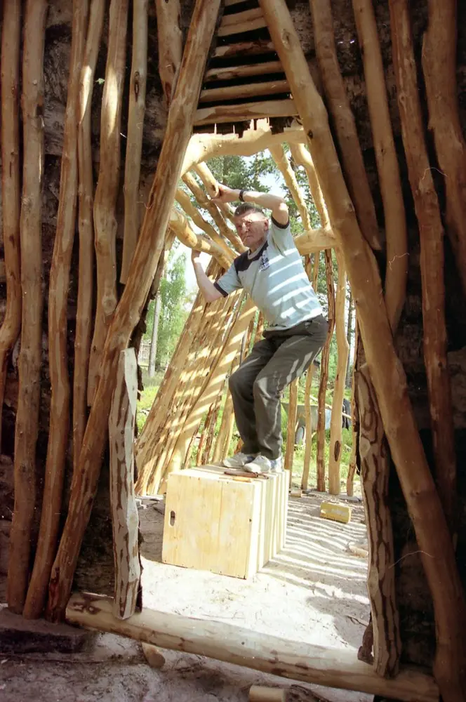 Vi ser gjennom døra, ut fra gamma og inni gangen, hvorJonas Danielsen setter opp bjørkestenger i gangen.
