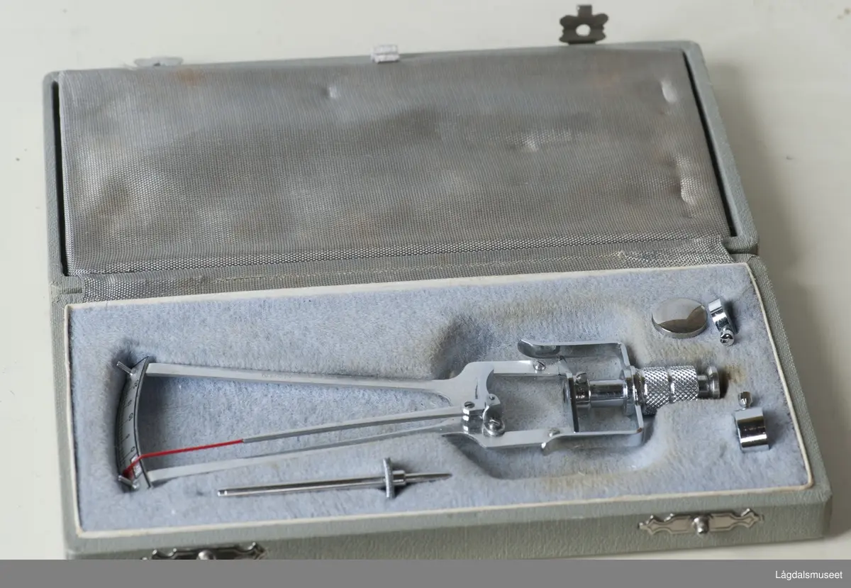 Etui som inneholder et tomometer, en løs pendelspiss, samt to forskjelige vekter til å feste til instrumentet. Etuiet er delt i to. I dene ene delen ligger det beskrevne instrument. I det andre rommet ligger en godkjenning "Certificate of accuracy for Schioets Tonometer". Dette er et stivt ark/kartong med  diverse referanserammenr for instrumentet,  markert med punktene 1 - 25. Inne i dette sertifikatet ligger en lapp som er skrevet på norsk og som viser at tonometer nr 1659 er godkjent av Tonometerkontrolstasjonen, Øyeavdelingen, Bergen, datert 25/9-67, signert H. Aasved. I det samme rommet ligger også et skjema hvor det er skrevet inn, for hånd, resultatene fra en tonometerkontroll. Standardverdiene er maskinskrevet til høyre på arket.. Skjemaet er undertegnet Tonometerkontrolstasjonen,  Oftalmologisk avd., Universitetet i Bergen, datert 25/9-67, signert H. Aasved. I samme rommet ligger en avreven og håndskreven lapp med innskriften "Til å måle trykk i øyet". I det samme rommet ligger det to piperensere. Etuiet er i tre/papp, trukket med stoff. Innvendig er det kledd med fløyel i rommet hvor instrumentet ligger. Etuiet har blanke hengsler, samt "snirklete" lås/lukkebeslag som også er blanke.