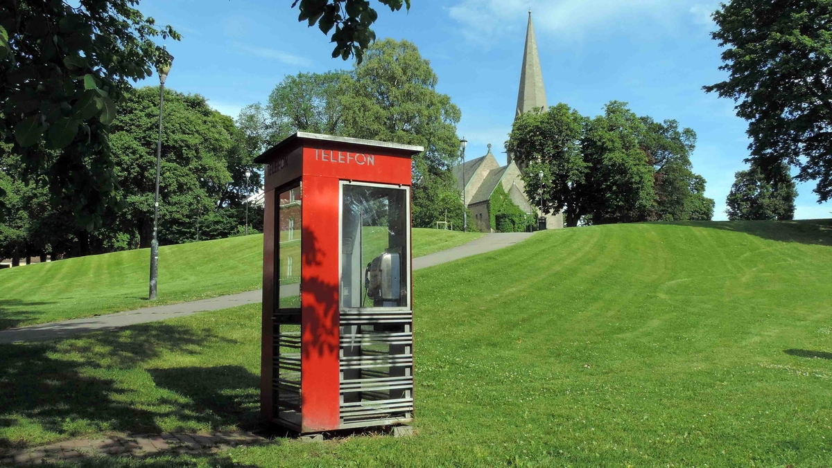 This is the story of how Norway’s most important conversation-space was designed by a young, freshly graduated man from Bergen.

“Norwegian architects are hereby invited…”
In the autumn of 1932, Oslo Telefonanlegginitiated an architectural competition. Finally, Oslo would get its own telephone booth. The city had had so called “talking-stations” from 1885, which in turn were overtaken by automatic telephones 
 only available at selected Narvesen kiosks. The state 
was of the opinion that now was the time to offer the public a better service; public telephone booths open 24/7, like the ones they already had in Sweden and England. But what would they look like, these new telephone booths? What considerations would it
 be necessary to take when designing it? The telegraph board developed a detailed list of demands and restraints: “The booth is intended to be placed outside on the streets and squares and need to be designed so that snow and ice does not hinder the opening and closing of the doors,” they wrote. “To prevent vandalism, theft, uncleanliness etc. inside the booth, it needs to be designed so that from all angles one may see what is going on in there.” Additionally, it would need to withstand storms and bad weather, and “preferably also being whipped by rain mixed with seawater” 

This was not all: The appearance would have to be «pleasing». The booth also needed to be movable, so that it could be taken in to be serviced at Telegrafverket’s main workshops. The reqired material was iron, and the surface was to be spray painted  preferably using car-body paint. There was a requirement for “a writing shelf, a pack shelf, and a suitable place for the telephone catalogue.” Also, there would need to be an illuminated TELEFON  sign, easily visible from all four angles. The total cost for each booth should not exceed 1000 kroner. The first prize for coming up with such a product was 800 kroner.

“Norwegianarchitects are hereby invited to partake in a competition for the design of a telephone booth…”  

The man with the solution
«At some point in 1932, Georg Fredrik sat at a party in Bergen. Maybe he felt a bit lost and forgotten as he often had throughout his life. He retreated to a quiet corner, took out a pencil and strted doodling on a matchbox.  According to my mother, this was how the telephone booth came into being.” In the book “Norges lille røde  historien om telefonkiosken,” Lars Fasting describes his father, the man who is far less known than the iconic architctural structure he left behind. Georg Fredrik Fasting was from Bergen, born into a family of working people and smallholders. One unusual facet of Georg Fredrik was that he was born without ears. His mother made sure he learnt to speak, read and write, 
ut Lars Fasting indicates that his father would seek refuge in drawing when the social challenges became too much to bear. And in the end drawing became his profession. In 1924 he secured a guarantor for a student loan, and started studying to become an a
rchitect at the NTH. Throughout the 1930s he entered several architectural competitions, with drafts produced, according to his son, “after work and in the late hours of the night.”

His efforts were not wasted. Out of 93 entries, with names such as “Flirt”, “Brrr”, “Ring” and “Amor”, the jury selected Fasting’s submission, “RIKS” as the new telephone booth: “The draft shows a strikingly simple solution to the task, technically as well as aesthetically well worked out.”

Taut and provident
Simple and aesthetc are the keywords here. Fasting had designed a booth pointing towards the future, and to modernism. Just how modern it was can be seen by comparing RIKS to the British telephone booth, also designed in the interwar-era. While the British version with it classicistic style is looking back to the heyday of the empire, Fasting’s booth is progressive and functionalistic. Like most Norwegian architects, Fasting broke with the classicistic style of architecture after the Stockholm-exhibition in 1930. “After it, almost all buildings erected in Norway until the German invasion in 1940, were in the functionalistic architectural style,” writes senior curator of architecture at the Norwegian National Museum, Ulf Grønvold, in the book, “Den lille røde”.“TheNorwegian booth is a piece of functionalistic architecture, an asymmetric composition with its roof slab overhanging the word TELEFON, in bold sans seraph lettering,”concludes Ulf Grønvold.

Fashionably red
And it was red. Fasting chose a colour which was part of the modern palette. “A bright red colour, but not as shiny as a signal red, the character of the colour places it among the fashionable colours within functionalism,” states paintings conservator and researcher in NIKU (Norwegian Institute for Cultural Heitage Research), Jon Brænne. In his opinion, Fasting went for visibility without making the booth stand out too much from its surroundings. The original colour was in use up to around 1950, when it changed to signal red. Towards the end of the 1970s the clour was again adjusted towards today’s orangey red.

The design, however, has not changed. RIKS is eighty years and still looks remarkably good. That’s what makes Fasting’s telephone booth a classic  even before it was added to DOCOMOMO’s list over moden icons of design. For Telenor, the telephone booth has served as a pathway into the hearts of the public. For many, Telenor (Televerket) was synonymous with exactly this telephone booth, because this was where one would go to place a call. Having a home
phone was not common until the 1980s. As such the red box became part of the Norwegian everyday and consciousness. The symbol- and publicity value of this is hard to evaluate, but in 2007 it was time to give honour where honour was due, Telenor, in consul
tation with the Directorate for Cultural Heritage, decided to preserve 100 telephone booths for all eternity.

And what about Georg Fredrik Fasting? What happened to him? At the age of 56 an entry in his diary states: «I CAN HEAR». As the first person in th world he had undergone an operation where he had ear canals constructed and eardrums fitted. For the rest of his life, the man behind Norway’s own telephone booth could answer the telephone himself.

Source: Norges lille røde historien om telefonkiosken (2007), issued by The Norwegian Telecom Museum and Telenor Cultural Heritage.