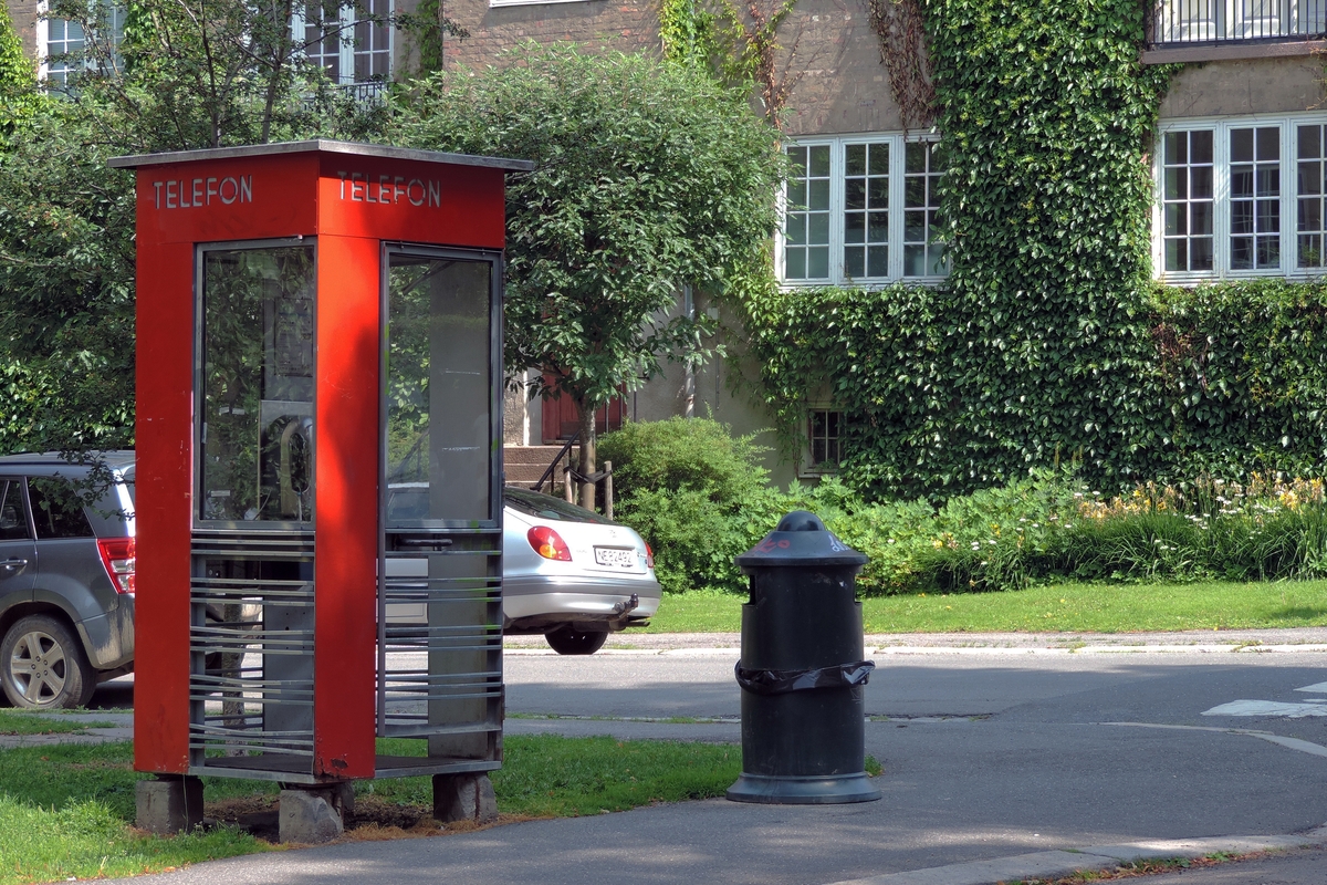 This is the story of how Norway’s most important conversation-space was designed by a young, freshly graduated man from Bergen.

“Norwegian architects are hereby invited…”
In the autumn of 1932, Oslo Telefonanlegginitiated an architectural competition. Finally, Oslo would get its own telephone booth. The city had had so called “talking-stations” from 1885, which in turn were overtaken by automatic telephones 
 only available at selected Narvesen kiosks. The state 
was of the opinion that now was the time to offer the public a better service; public telephone booths open 24/7, like the ones they already had in Sweden and England. But what would they look like, these new telephone booths? What considerations would it
 be necessary to take when designing it? The telegraph board developed a detailed list of demands and restraints: “The booth is intended to be placed outside on the streets and squares and need to be designed so that snow and ice does not hinder the opening and closing of the doors,” they wrote. “To prevent vandalism, theft, uncleanliness etc. inside the booth, it needs to be designed so that from all angles one may see what is going on in there.” Additionally, it would need to withstand storms and bad weather, and “preferably also being whipped by rain mixed with seawater” 

This was not all: The appearance would have to be «pleasing». The booth also needed to be movable, so that it could be taken in to be serviced at Telegrafverket’s main workshops. The reqired material was iron, and the surface was to be spray painted  preferably using car-body paint. There was a requirement for “a writing shelf, a pack shelf, and a suitable place for the telephone catalogue.” Also, there would need to be an illuminated TELEFON  sign, easily visible from all four angles. The total cost for each booth should not exceed 1000 kroner. The first prize for coming up with such a product was 800 kroner.

“Norwegianarchitects are hereby invited to partake in a competition for the design of a telephone booth…”  

The man with the solution
«At some point in 1932, Georg Fredrik sat at a party in Bergen. Maybe he felt a bit lost and forgotten as he often had throughout his life. He retreated to a quiet corner, took out a pencil and strted doodling on a matchbox.  According to my mother, this was how the telephone booth came into being.” In the book “Norges lille røde  historien om telefonkiosken,” Lars Fasting describes his father, the man who is far less known than the iconic architctural structure he left behind. Georg Fredrik Fasting was from Bergen, born into a family of working people and smallholders. One unusual facet of Georg Fredrik was that he was born without ears. His mother made sure he learnt to speak, read and write, 
ut Lars Fasting indicates that his father would seek refuge in drawing when the social challenges became too much to bear. And in the end drawing became his profession. In 1924 he secured a guarantor for a student loan, and started studying to become an a
rchitect at the NTH. Throughout the 1930s he entered several architectural competitions, with drafts produced, according to his son, “after work and in the late hours of the night.”

His efforts were not wasted. Out of 93 entries, with names such as “Flirt”, “Brrr”, “Ring” and “Amor”, the jury selected Fasting’s submission, “RIKS” as the new telephone booth: “The draft shows a strikingly simple solution to the task, technically as well as aesthetically well worked out.”

Taut and provident
Simple and aesthetc are the keywords here. Fasting had designed a booth pointing towards the future, and to modernism. Just how modern it was can be seen by comparing RIKS to the British telephone booth, also designed in the interwar-era. While the British version with it classicistic style is looking back to the heyday of the empire, Fasting’s booth is progressive and functionalistic. Like most Norwegian architects, Fasting broke with the classicistic style of architecture after the Stockholm-exhibition in 1930. “After it, almost all buildings erected in Norway until the German invasion in 1940, were in the functionalistic architectural style,” writes senior curator of architecture at the Norwegian National Museum, Ulf Grønvold, in the book, “Den lille røde”.“TheNorwegian booth is a piece of functionalistic architecture, an asymmetric composition with its roof slab overhanging the word TELEFON, in bold sans seraph lettering,”concludes Ulf Grønvold.

Fashionably red
And it was red. Fasting chose a colour which was part of the modern palette. “A bright red colour, but not as shiny as a signal red, the character of the colour places it among the fashionable colours within functionalism,” states paintings conservator and researcher in NIKU (Norwegian Institute for Cultural Heitage Research), Jon Brænne. In his opinion, Fasting went for visibility without making the booth stand out too much from its surroundings. The original colour was in use up to around 1950, when it changed to signal red. Towards the end of the 1970s the clour was again adjusted towards today’s orangey red.

The design, however, has not changed. RIKS is eighty years and still looks remarkably good. That’s what makes Fasting’s telephone booth a classic  even before it was added to DOCOMOMO’s list over moden icons of design. For Telenor, the telephone booth has served as a pathway into the hearts of the public. For many, Telenor (Televerket) was synonymous with exactly this telephone booth, because this was where one would go to place a call. Having a home
phone was not common until the 1980s. As such the red box became part of the Norwegian everyday and consciousness. The symbol- and publicity value of this is hard to evaluate, but in 2007 it was time to give honour where honour was due, Telenor, in consul
tation with the Directorate for Cultural Heritage, decided to preserve 100 telephone booths for all eternity.

And what about Georg Fredrik Fasting? What happened to him? At the age of 56 an entry in his diary states: «I CAN HEAR». As the first person in th world he had undergone an operation where he had ear canals constructed and eardrums fitted. For the rest of his life, the man behind Norway’s own telephone booth could answer the telephone himself.

Source: Norges lille røde historien om telefonkiosken (2007), issued by The Norwegian Telecom Museum and Telenor Cultural Heritage.