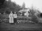 Justina Johansson på Huset och hennes dotter Ida, Krokstads socken i Sörbygden, fotograferade framför stengärdsgård, potatisodlingen och bostaden.