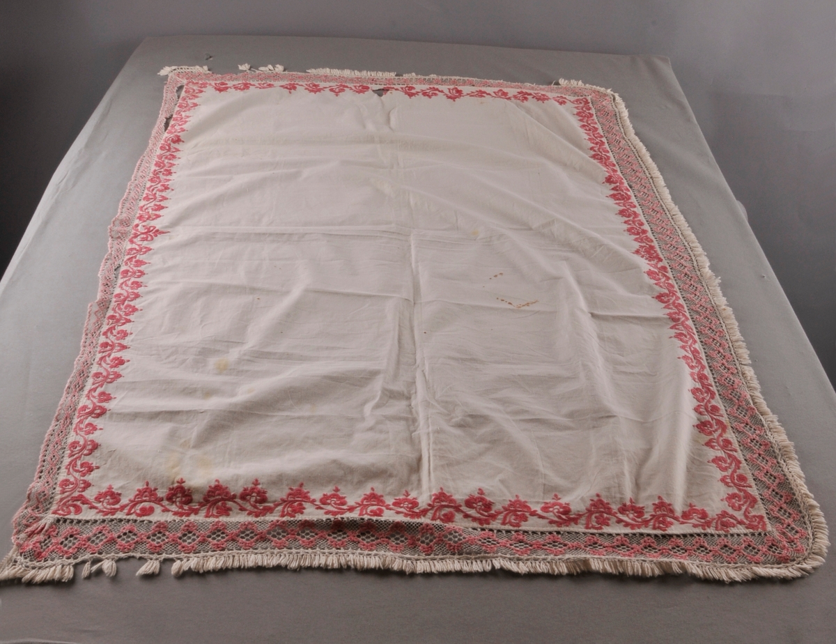 Rektangulært stykke av bomullslerret med rosa rosesaum kring alle sider. Ei påsauma kvit og rosa blonde i Telemarksbinding, i to ulike bredder, langs alle sidene.