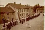 Logen Margareta i demonstrationståg på Stortorget i slutet av 1890-talet. Utanför Kappers raksalong står Kappers dotter Anina, syster till järnhandlare K.J. Wibergs fru, född Olga Kappers. Polisen är konstapel Norén. Vid x går den gamle nykterhetskämpen Hall. Alfr. Jonssons båda hus till vänster.