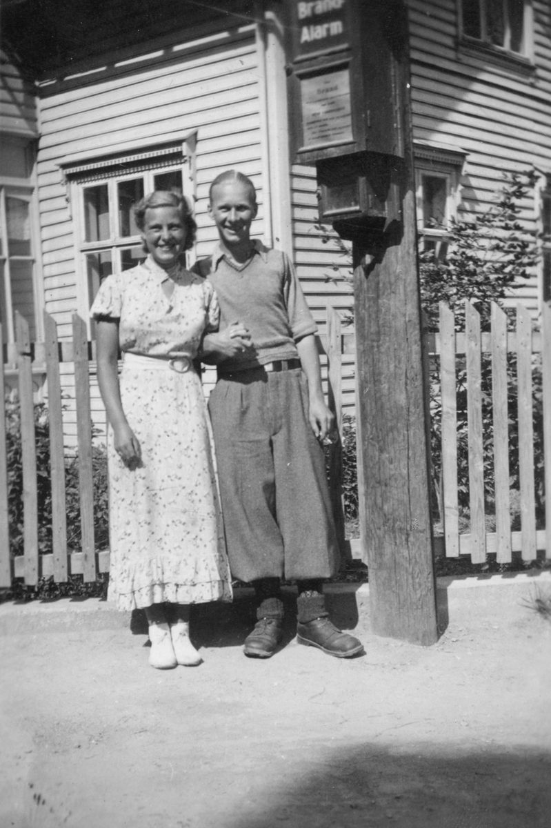 Mann og kvinne ved ein stolpe med brannalarm.
