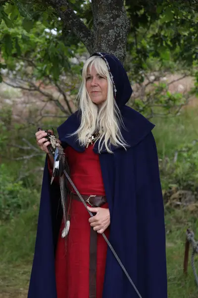 Dame i rød middelalderkjole og blå kappe. Hun holder en volvestav