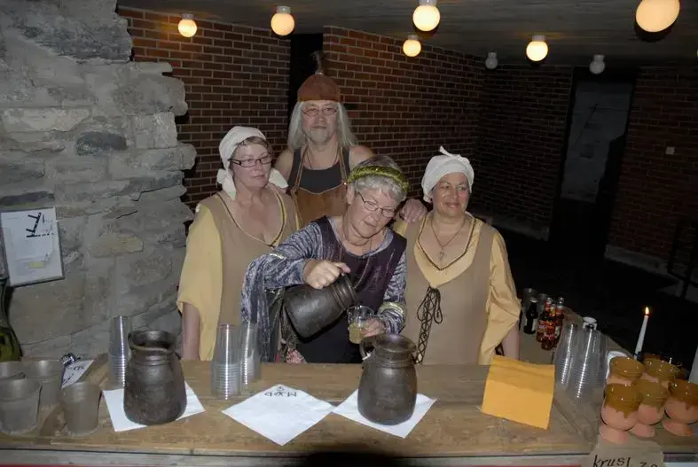 Tre damer og en mann i middelalderklær som står bak et bord med leirmugger og leirkrus