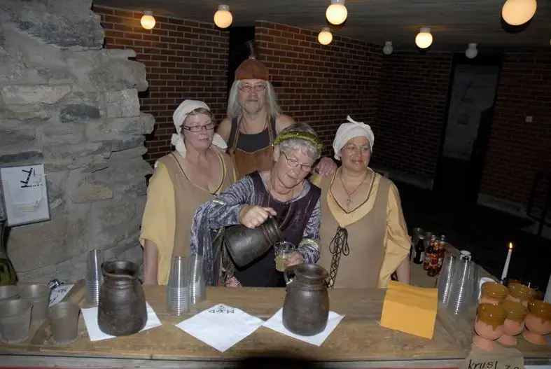 Tre damer og en mann i middelalderklær som står bak et bord med leirmugger og leirkrus