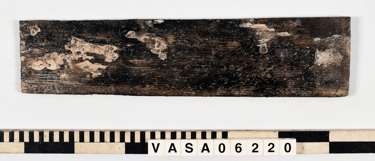 Avsmalnande bräda med två synliga spikhål. 
Lätt vittrad, tunt lager PEG.