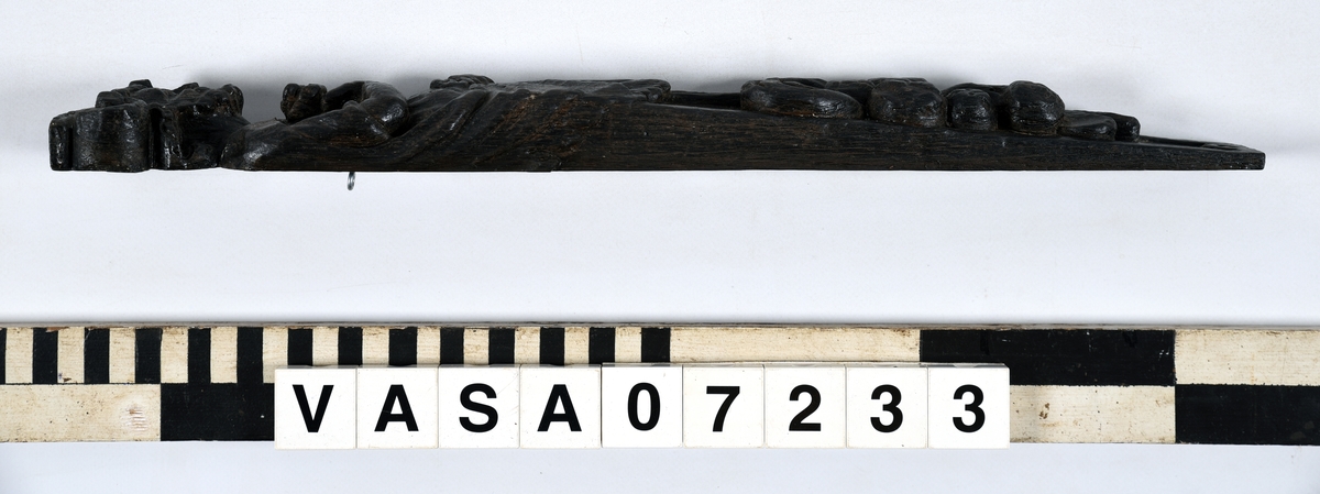 Hermpilaster.
Liten skulpterad pilaster föreställande skäggig herm under joniskt kapitäl.
Huvudet är vridet mot vänster. Hermen är insvept i en mantel som hålls fast med vänster hand framför magen. I höger hand håller figuren ett okänt föremål (blomsterkälk?) framför bröstet. Pilasterskaftet är prytt med stora frukter och blad, fasthängande vid en stängel som delvis täcker det nedåt avsmalnande skaftets ramverk. Baksidan är slät.
Skulpturen är mycket välbevarad med sju spikhål.

Text in English: Small sculpted pilaster with a bearded Herm beneath an Ionic capital.
The head of the figure is turned to the left. The Herm is enveloped in a mantle, held fast with the left hand in front of its stomach. Its right hand holds an unknown object (a bunch of flowers?) in front of its breast. The shaft of the pilaster is decked with large fruit and leaves hanging from a stalk which partly cover the framing of the tapering shaft. Its back is flat.
The sculpture is very well preserved.