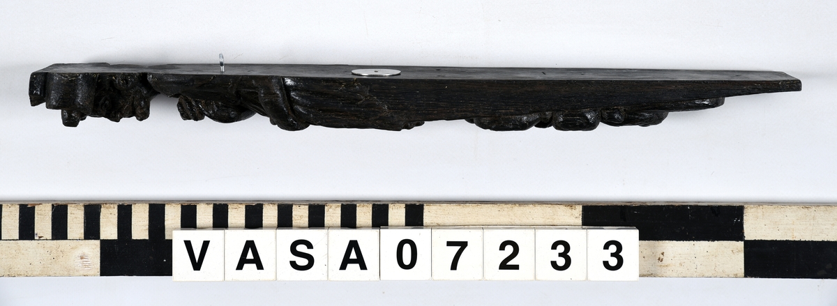 Hermpilaster.
Liten skulpterad pilaster föreställande skäggig herm under joniskt kapitäl.
Huvudet är vridet mot vänster. Hermen är insvept i en mantel som hålls fast med vänster hand framför magen. I höger hand håller figuren ett okänt föremål (blomsterkälk?) framför bröstet. Pilasterskaftet är prytt med stora frukter och blad, fasthängande vid en stängel som delvis täcker det nedåt avsmalnande skaftets ramverk. Baksidan är slät.
Skulpturen är mycket välbevarad med sju spikhål.

Text in English: Small sculpted pilaster with a bearded Herm beneath an Ionic capital.
The head of the figure is turned to the left. The Herm is enveloped in a mantle, held fast with the left hand in front of its stomach. Its right hand holds an unknown object (a bunch of flowers?) in front of its breast. The shaft of the pilaster is decked with large fruit and leaves hanging from a stalk which partly cover the framing of the tapering shaft. Its back is flat.
The sculpture is very well preserved.