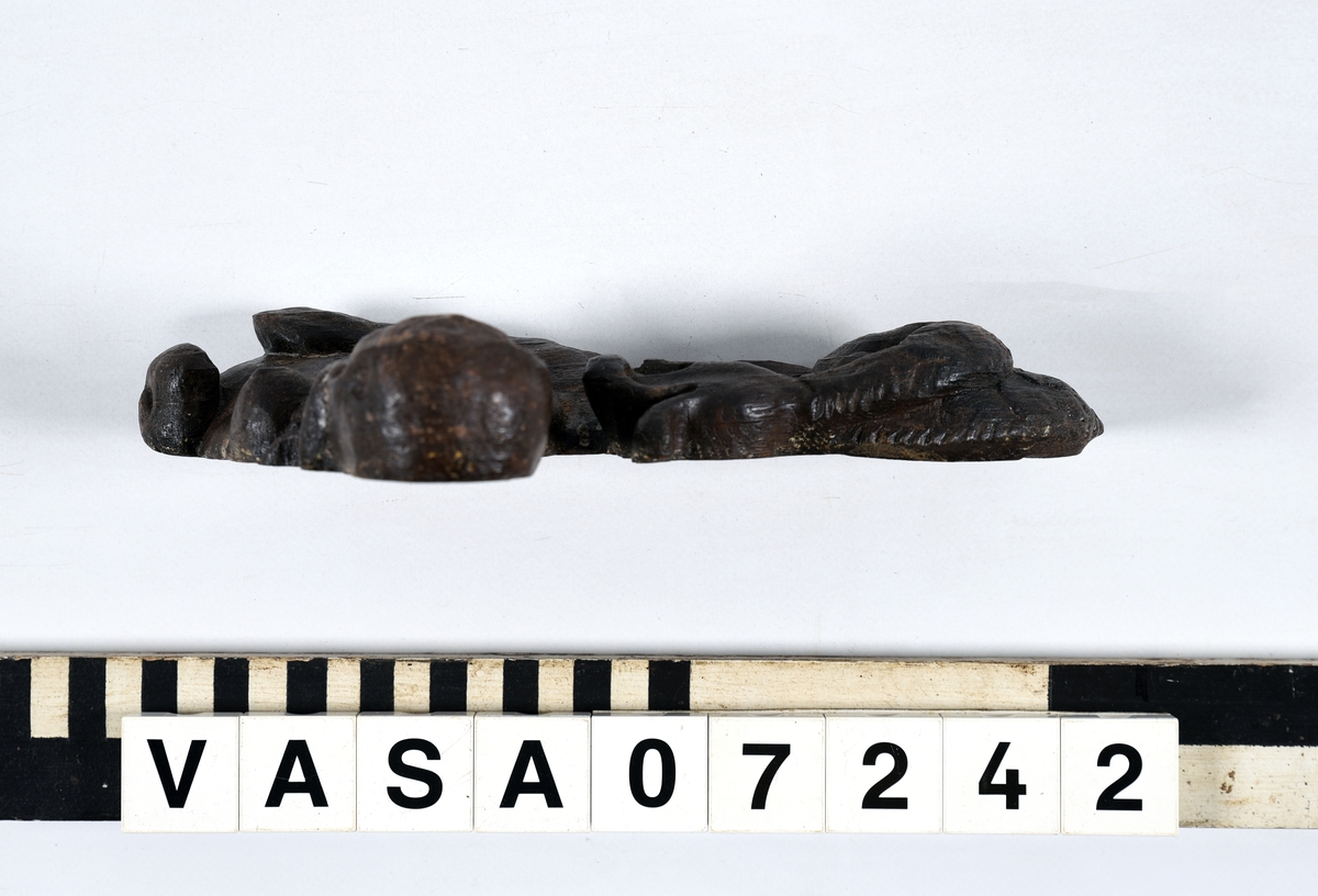 Sjöjungfru.
Liten sjöjungfru eller nereid, till hållningen erinrande om en sfinx, med kraftiga framben och upprullad fiskstjärt.
Kroppen är återgiven i höger profil med det något bakåtlutande huvudet en face. Det barnsligt knubbiga ansiktet inramas av långt hår. Runt halsen sitter ett snott band med en medaljong prydd med ett inristat kors. Baksidan är slät. Nederkanten och framkanten är rakskurna. Huvudet är snidat separat.
Skulpturen är mycket välbevarad, ansiktet är dock något slitet. På baksidan syns en spricka.

Text in English: Small sculpture of a mermaid or Nereid, posed like a sphinx, with powerful forelegs and a rolled-up fish tail.
The body is seen in right profile or half-profile with the head bent slightly backwards, en face. The chubby childish face is framed by long hair. There is a twisted ribbon round its neck, supporting a medallion decorated with a cross. The back is flat, and the lower and front edges are cut at right angles. The head is carved separately.
The sculpture is well preserved, although the face is somewhat worn. There is a crack on the reverse side.

Tre spikhål, ett som är dolt med en plugg på Sfinxens hals.