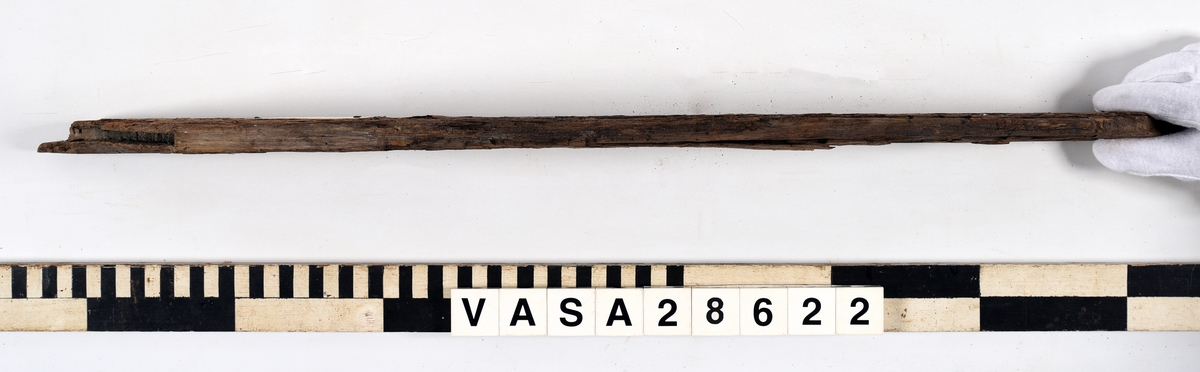 Odekorerad trapetsoid med spont på båda ändarna och sex spikhål, fem längsmed den längsta långsidan en på toppen av kortaste långsidan. Den ena sponten är helt avbruten. Torr och flagnande yta.