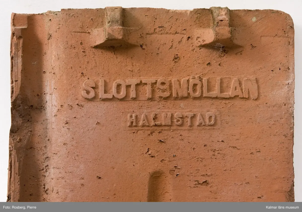 KLM 44570:1 Taktegel, av tegel. Falstaktegel, oglaserat, formpressat, oskadat. Stämplat på undersidan: Slottsmöllan Halmstad. Tillverkad av Slottsmöllans tegelbruk.
