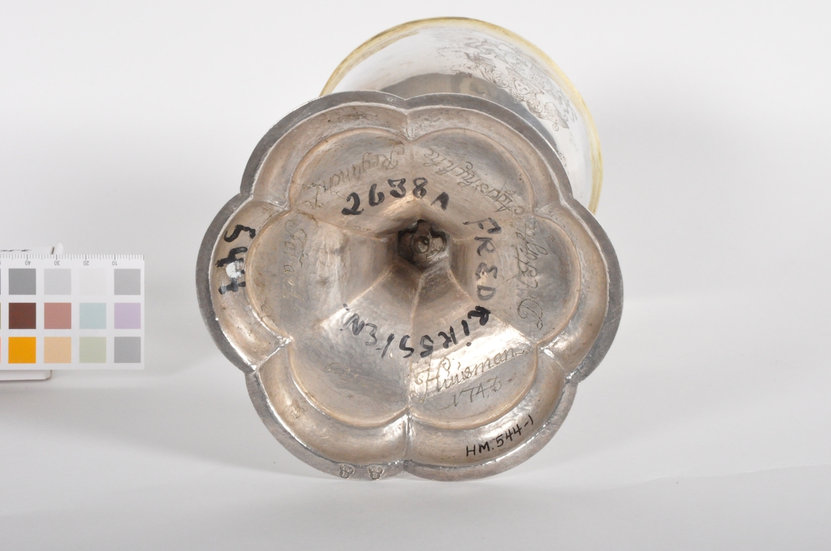 Alterkalk i sølv. Begeret er enkelt utformet med glatte sider og har innrisset som dekor et våpenskjold (antatt Hausmanns). Stetten er sekskantet og avbrutt av en disk som stikker ca 2 cm utenfor stetten. Under disken har stetten en dekorativ bård med to buedne fliker på hvar flate på stetten. Stetten ender opp i en fot som er formet som en blomst med seks kronblader.