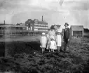 Familjegrupp fem personer. Bostadshus och fabriksbyggnader i  bakgrunden.
Troligen Emilia Johansson med döttrarna Ingeborg, Brita och Hedvig. Mannen är hennes make Karl Johansson.
Bilden tagen före mars 1915 då Hedvig dog.
Platsen Örebro ? Hallsberg?
Se även bild 17.