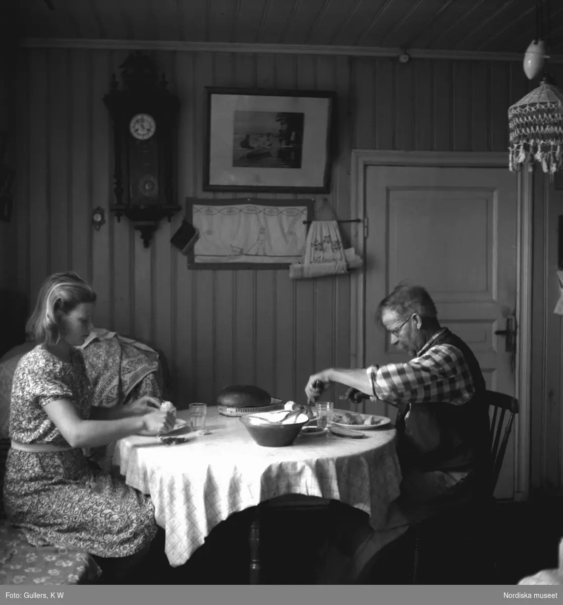 Uppdukat med sill och potatis . Den unga kvinnan bär en modern klänning av mönstrat tryckt tyg, och mannen en rutig arbetsskjorta. På väggen hänger en klocka i nyrenässansstil från sekelskiftet 1900 och en bonad som med stor sannolikhet är broderad av kvinnorna i familjen under lediga stunder. 

Läs mer om interiören och föremålen under rubriken Övrig information