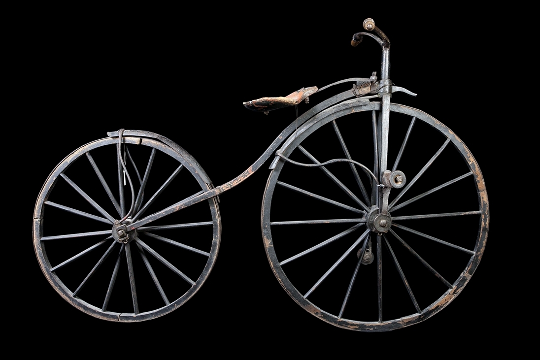 Cykel, Michaux-typ av järnsmide. Avancerad typ. Svagt S-formig ram med högt uppdraget styrrör och skålformig sits av trä, på separat fjäderblad. Bakåtsvept styrstång med åt sidorna rakt utstående handtag av furu. Stänkskärmar. Järnskodda hjul av trä på dubbel rad ekrar. Trampor av trä, på järnaxlar, justerbart fastskruvade i vevar, direkt verkande på framaxeln. Svart med röd sits.