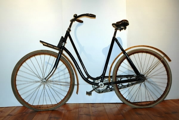 Cykel, dammodell av stålrör. Sadel, läder, i plåtram på spiralfjädrar. Styrstångshandtag av trä. Ringklocka. Pakethållare fäst till styrröret med bultklammer. Träfälgar. Däck av märket TINGVALLA. Suspensionsekrar. Stänkskärmar av trä, den bakre med hål för fästande av kjolnät. Hel vev. Kedja av 2,4 cm långa länksidor, alla med oval mittöppning, förenade genom massiva mellanstycken. Kedjeskydd av plåt genombrutet i cirkelmönster. Svart med förkromat styre. Fälgar och stänkskärmar oljestrukna. På styrrörets framsida korsformig kartusch i vitmetall mellan två nymånar vända mot varandra. Märkning: "N:o 12, CRESCENT, WESTERN WHEEL WORKS, CHICAGO, U.S.A"