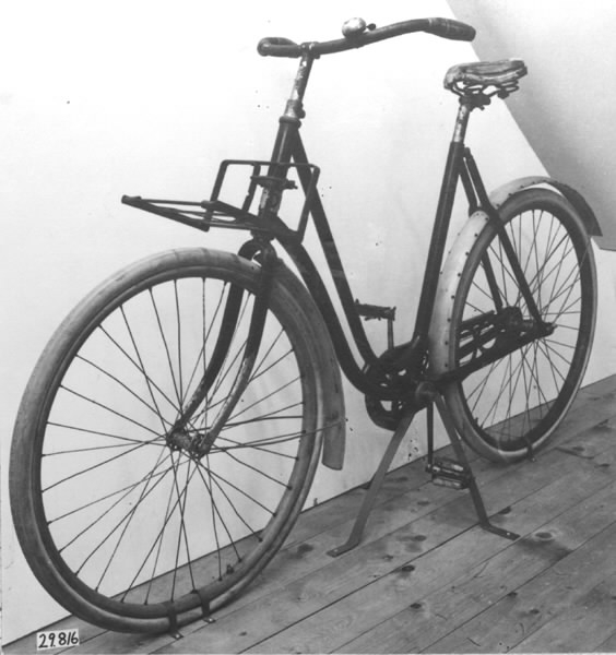 Cykel, dammodell av stålrör. Sadel, läder, i plåtram på spiralfjädrar. Styrstångshandtag av trä. Ringklocka. Pakethållare fäst till styrröret med bultklammer. Träfälgar. Däck av märket TINGVALLA. Suspensionsekrar. Stänkskärmar av trä, den bakre med hål för fästande av kjolnät. Hel vev. Kedja av 2,4 cm långa länksidor, alla med oval mittöppning, förenade genom massiva mellanstycken. Kedjeskydd av plåt genombrutet i cirkelmönster. Svart med förkromat styre. Fälgar och stänkskärmar oljestrukna. På styrrörets framsida korsformig kartusch i vitmetall mellan två nymånar vända mot varandra. Märkning: "N:o 12, CRESCENT, WESTERN WHEEL WORKS, CHICAGO, U.S.A"