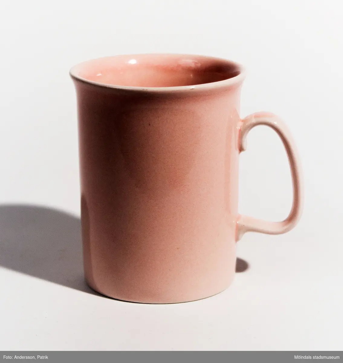 En rosa mugg med öra, tillverkad under 1980-talet. I botten står MADE IN ENGLAND. Materialet är i porslin med rosa glasyr.