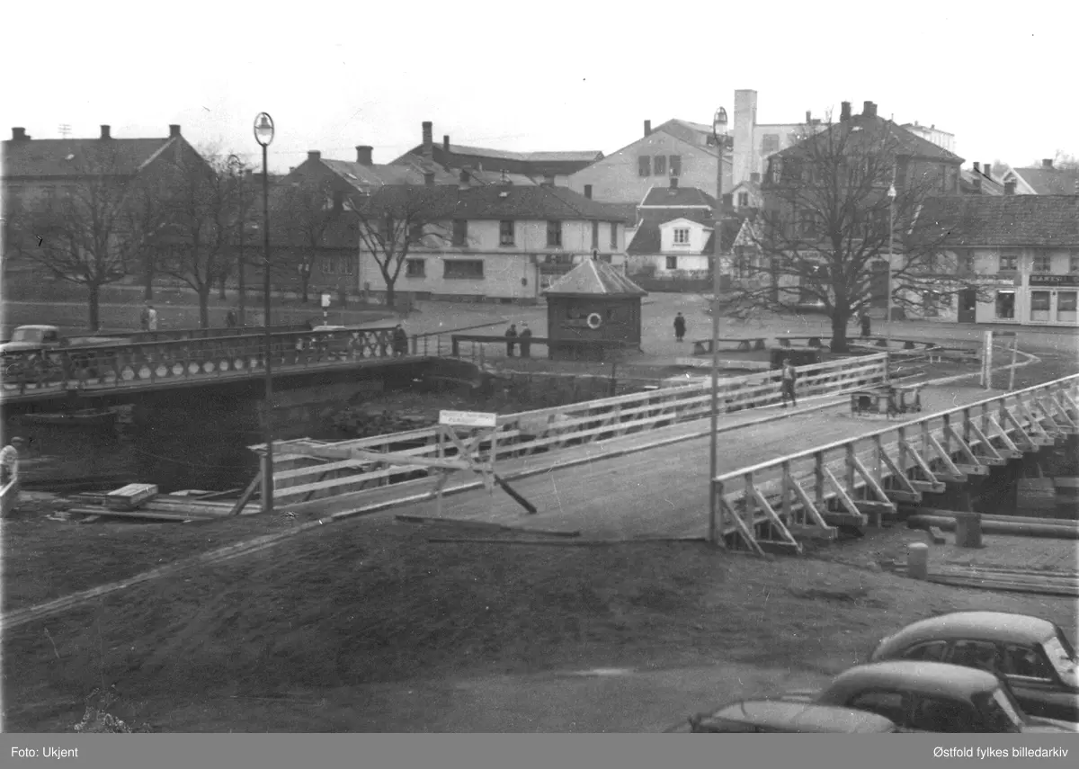 Kanalen i Moss.  Kanalbrua. Bruvakthuset i midten, kanalen sin provisoriske trebru ca. 1953. Riis-gården ses i bakgrunnen. 

Fra Moss Byleksikon:
Dagens bro skulle bygges på samme sted som den forrige, som ble stengt i 1953 etter 75 år. Derfor ble det i desember 1953 laget en midlertidig trebro på nordsiden, der broen hadde vært i perioden 1855-88. 
Kommentar: 
På bildet er den gamle fortsatt i bruk og den midlertidige brua åpnet for trafikk ennå. Bilen nærmest Kanalen er en Standard Vanguard 1948-1953-modell, sikkert klargjort på Den norske Automobilfabrikks anlegg på Kambo. (Ivar Stav 2016)
