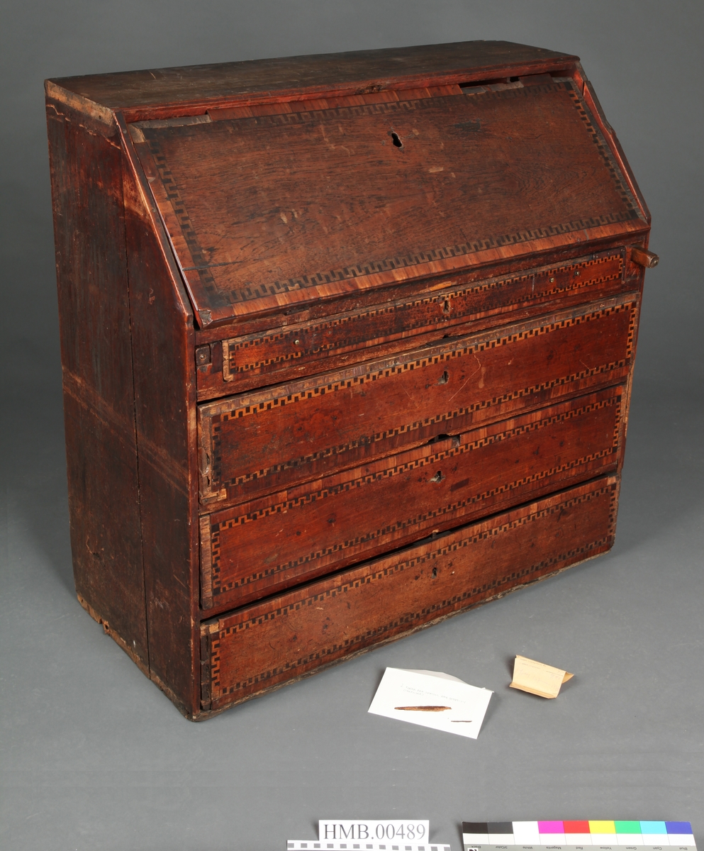 Lyst, rektangulært "slangebuktende" båndt med mørke felter i en bord langs tre sider av skriveplatens front og langs alle sidene av de tre store skuffene og den smale store skuffen.