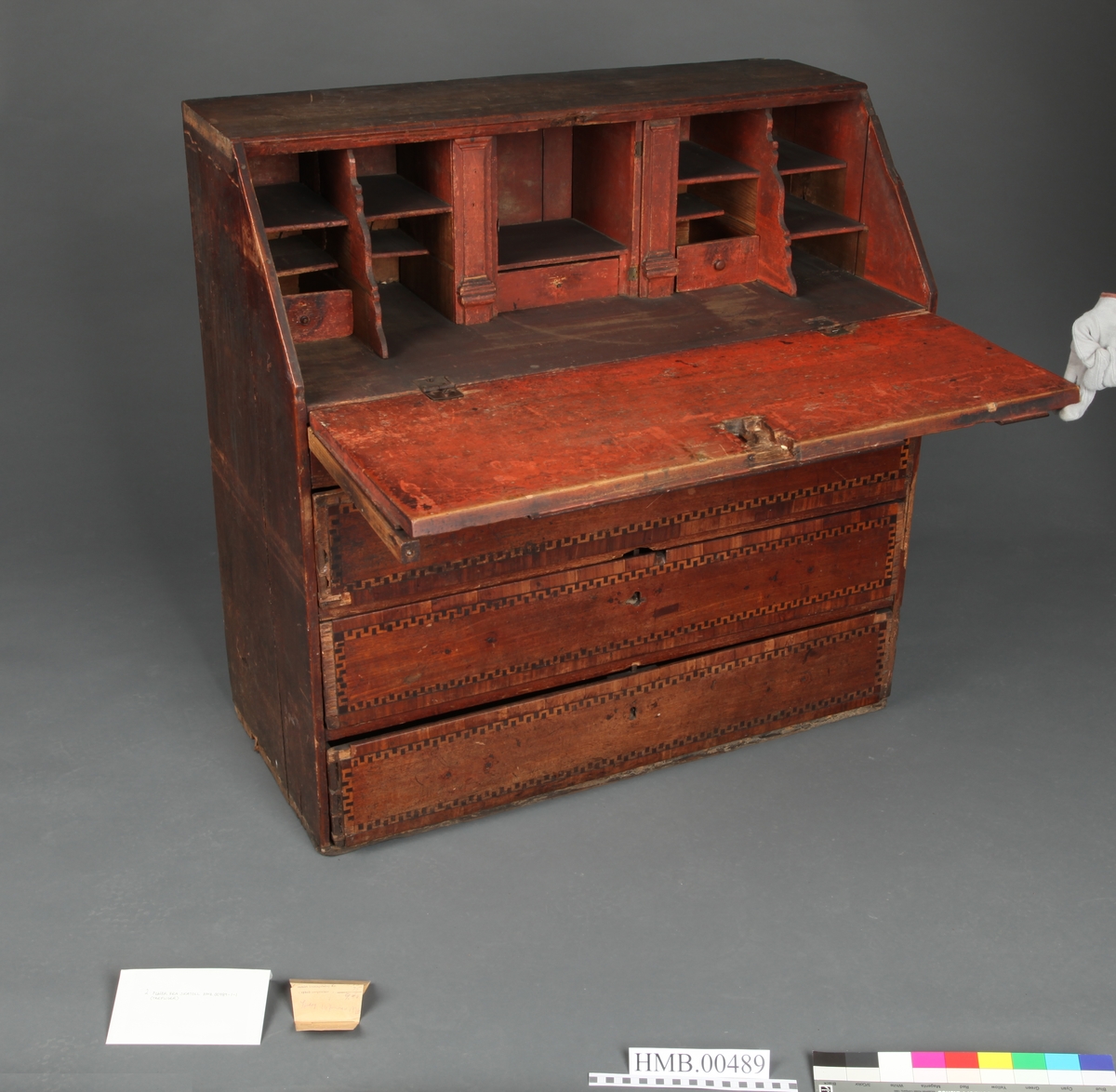 Lyst, rektangulært "slangebuktende" båndt med mørke felter i en bord langs tre sider av skriveplatens front og langs alle sidene av de tre store skuffene og den smale store skuffen.