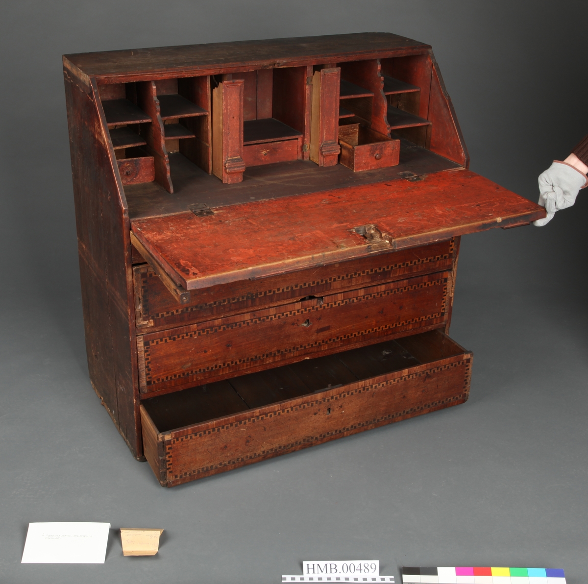 Lyst, rektangulært "slangebuktende" båndt med mørke felter i en bord langs tre sider av skriveplatens front og langs alle sidene av de tre store skuffene og den smale store skuffen.