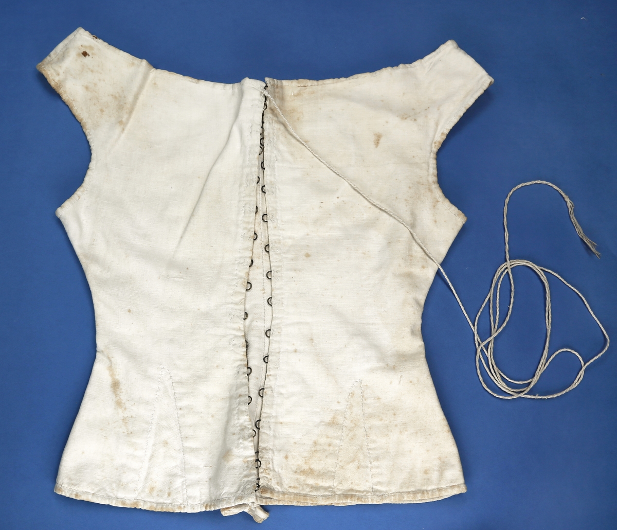 Liv eller korsett av lin med metallhekter og tvunnet tråd til snøring. Det har søm midt bak med hempe oppe og nede. Sidesømmen er litt tilbaketrukket, og det er felt inn stoff neders i sida for utsving fra livet. Halsåpningen er båtformet.