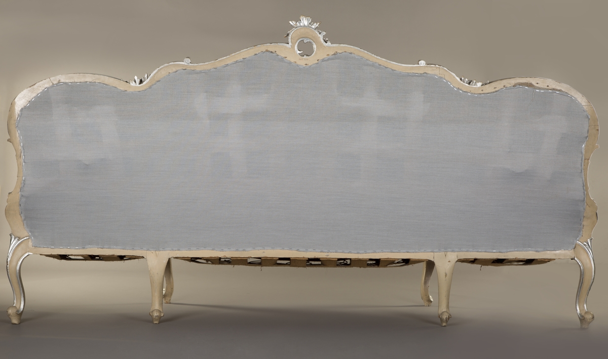 Sittemøbel for flere personer. Nyrokokko. Canapé à confidente - type, d.v.s. på hver side avsluttet av et sidesete. Alt treverk malt lyst grått med forsølvede ornamenter. Høy, stoppet rygg. Spiralfjærer både i sete og rygg. Trukket med tykk, rosa silke med ivevete, flerfargete blomster.
6 cabrioleben. de to forbena har øverst utskåret rocaille - lignende motiv med små blomster. Et glatt, åpent armlene på hver side av midtstykket.