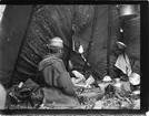 John Bauers Lapplandsresa sommaren 1904. I ett sameläger sitter en kvinna inne i kåtan med husgeråd omkring sig.
