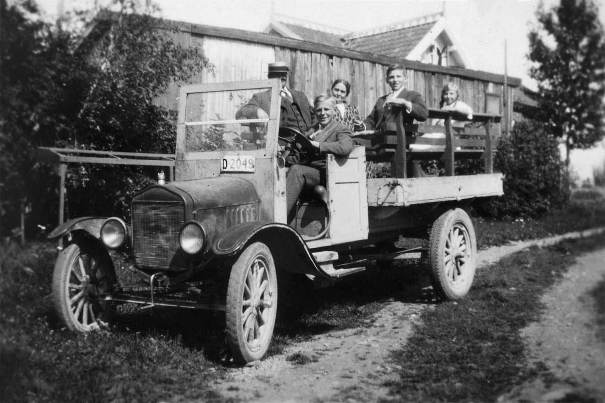 Gruppe 5 personer sittende i en Ford lastebil med reg.nr. D-2049. Kjøpt av O.M. Røe 25/4-1928 for 275 kr.