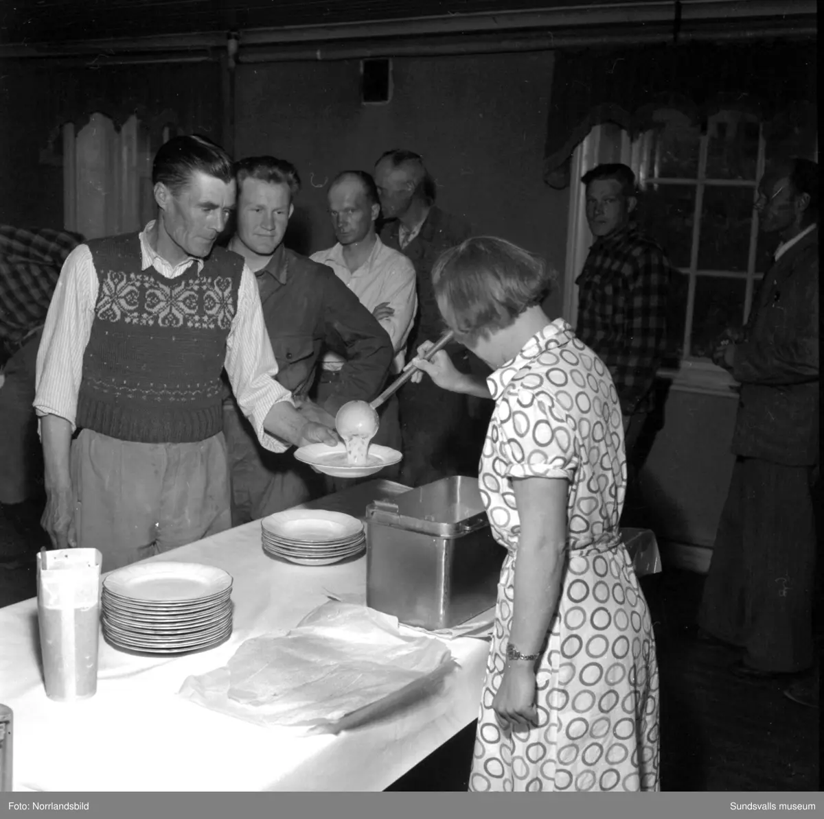 Sommaren 1951 anlände tolv finländska arbetare med båten Ragne till Sundsvall för att jobba vid Ortvikens sulfitfabrik. En välkommen förstärkning i tider då det var ont om arbetskraft. Som tillfällig förläggning användes Skönsbergs Folkets hus där den så kallade B-salen förvandlats till logement med tältsängar och i D-salen en trappa ned serverades maten. På den första bilden är det plåtslagaren Urhi Karlsson från Gamla Karleby som serveras spenatsoppa av Helga Rödén. På bild tre är det Eino Havu från Björneborg, till höger, som byter om efter sin första arbetsdag vid Ortviken.
