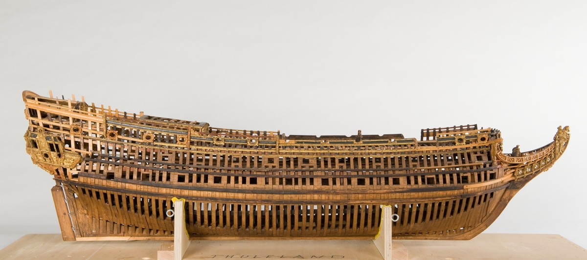 This unplanked model of a three-decker can be dated to c. 1660 and is one of the world's oldest models of a warship. Although not definitively identified, recent research links it to the Swedish ship *Riksäpplet*, designed by the English master shipwright Francis Sheldon and launched in 1661.     
The model was possibly made for Sheldon, who came to Sweden in 1659. He was one of a number of English shipwrights employed by the Swedish crown during the period. Previously, most Swedish warships had been built in the Dutch style.

From around 1660, the English Royal Navy’s administrators commissioned models that were accurately detailed and true to scale. These miniatures, which came to be called Navy or Admiralty Board models, had an unplanked lower hull to emphasise the shape of the underwater body. 

The model was restored by rear-admiral Jacob Hägg in the late 1890s. Missing parts have been reconstructed using lighter coloured wood.

3D model produced by Adam de Kaminski and Vasilis Haroupas for SMTM, 2023
