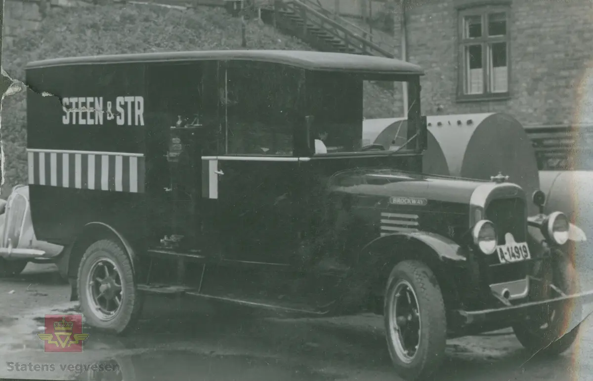 "Karbidgenerator produsert av Øveråsens Motorfabrikk, Gjøvik. De ble montert av Colbjørnsens & Co. A/S under hele krigstiden." I følge merking i album. På bilen med kjennetegn C-12178 står det skrevet "A/S Norske Konfektionsfabriker." På skiltet øverst på murbygningen står sannsynligvis "A/S Sveiseindustri." 

Bilde 1/4 er en Chevrolet med en eldre Chev. baklykt  på taket. 20.08.2016: "Bilde 1 er en Chevrolet 1939-40 varebil med norskbygd karosseri. "25.06.2018: Til venstre snuten av en Packard fra sent 1930-tall. Opplysninger fra Ivar Erlend Stav.
Klikk på pilen til høyre:
Bilde 2/4 er en Dodge 1935-1936 modell. (Strømmenbygd?)
Bilde 3/4  er en 1930 modell Brockway. 25.06.2018: Bildet 3 viser snuten av en Plymouth1937. Opplysninger fra Ivar Erlend Stav.
Bilde 4/4 er en Ford fra 1937-1938 modell." 25.06.2018:  "Ford 1938, siden det var første år med langsgående blanklist hos Ford. Karosseriet er originalt amerikansk varebilkarosseri på personbilchassis ("sedan delivery" - i motsetning til et mer grovbygd varekarosseri på lett lastebilchassis og lastebilfront, kalt "panel delivery". Opplysninger fra Ivar Erlend Stav. 

17.08.2016: Opplysninger til kjøretøyene på bildet v/tidligere daglig leder John Hindklev ved Norsk Kjøretøyhistorisk Museum. 

"Under andre verdenskrig besto virksomheten til firmaet Colbjørnsen stort sett av å montere og vedlikeholde karbidgeneratorer fra Øveråsen. Legg merke til hvordan man felte generatorene inn i varebilkarosseriene. Reklameteksten  ble delvis borte." Sitat fra boka: "Familiefirmaet-utenom allfarvei/2000 årsboken." Colbjørnsen & Co A/S, av Bjørn Ausjen Johannessen.