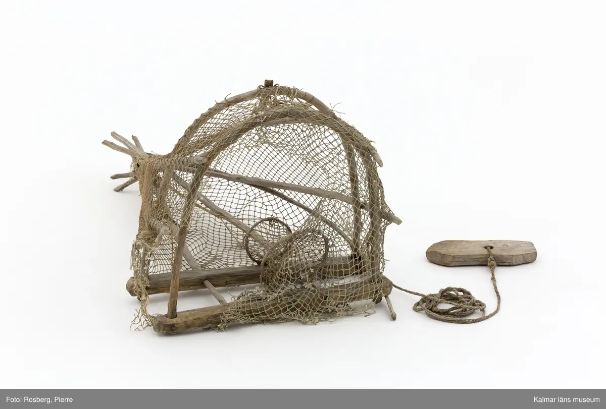 KLM 45863. Mjärde. Avlång fångstbur med stomme av trä och vidjor böjda till bågar med bundet nät av naturmaterial runt om. Även längsgående vidjor som i änden är hopknutna. Inuti en strutformad inredning med en ingång för fisken. På ovansidan ett fastbundet rep med en fastknuten träbit som fungerade som flöte.