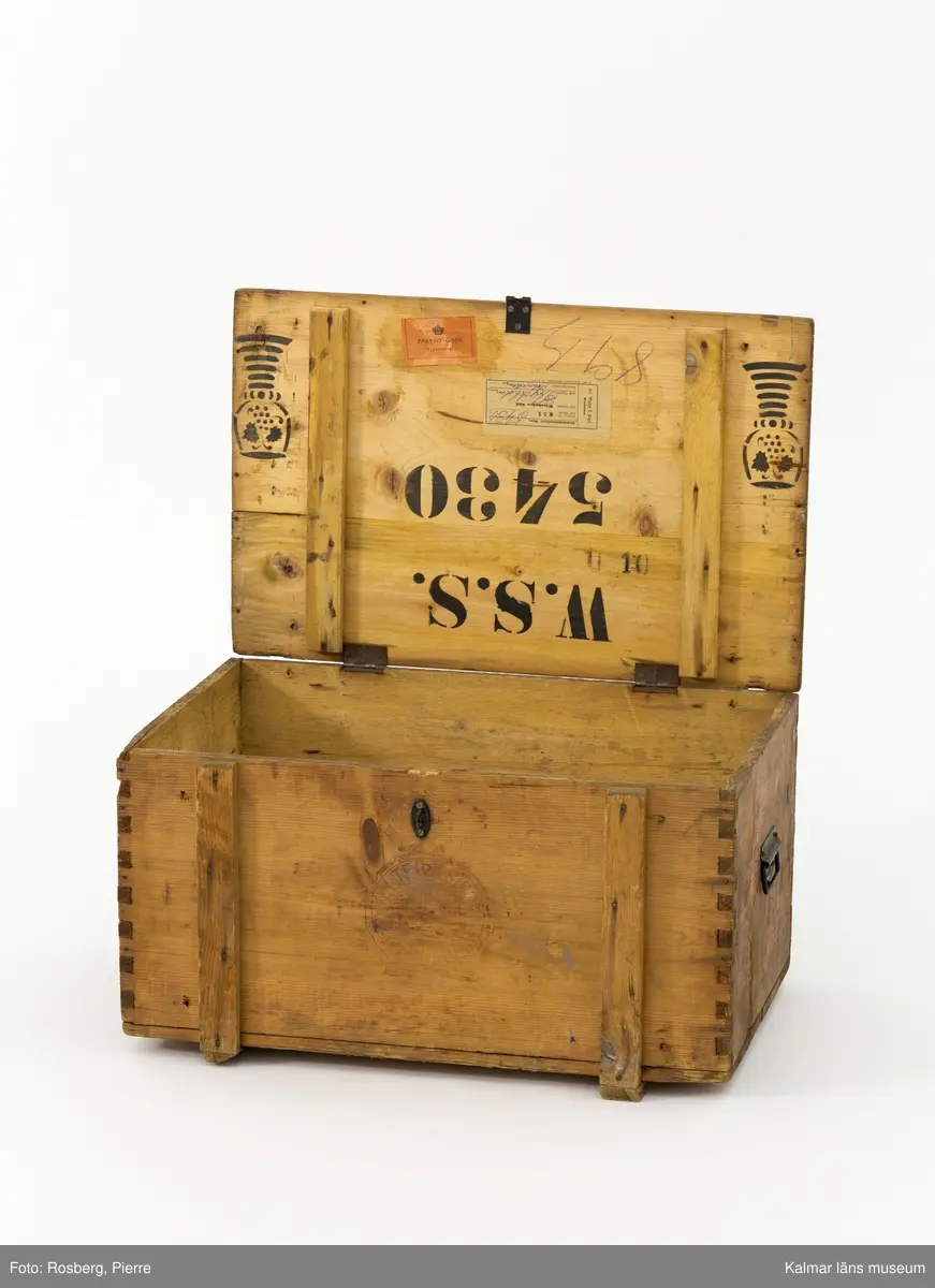 KLM 45273:74. Låda, av trä. Trälåda med lock. På gavlarna handtag av metall och på framsidan en bygel av metall där man kan stänga låda med ett hänglås.  På fram- och baksidan stämplad med ett emblem och texten Walter S Siegel Wiesbaden. På insidan är locket stämplat i svart med texten W.S.S. 5430 och två dekorerade remmare. På lockets insida sitter också två pappersetiketter klistrade. Den ena av vitt papper har text på tyska som berättar att lådan skickats från Wiesbaden till Stockholm. Den andra etiketten av rött papper har texten Transit-gods Trälleborg.