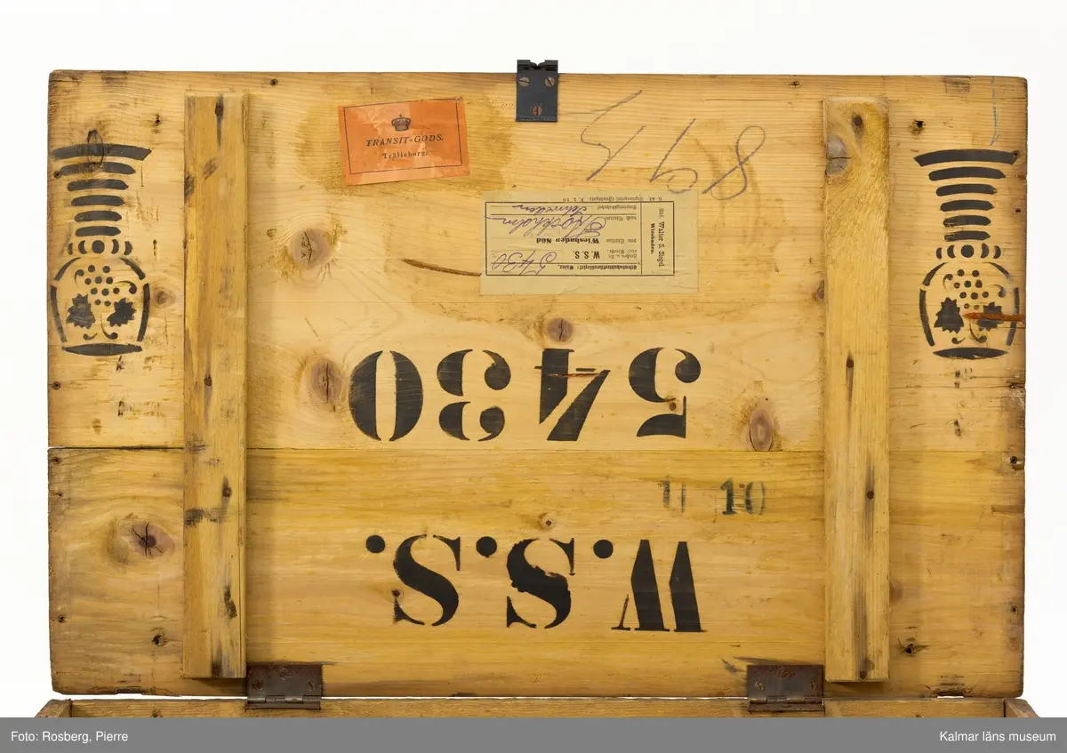 KLM 45273:74. Låda, av trä. Trälåda med lock. På gavlarna handtag av metall och på framsidan en bygel av metall där man kan stänga låda med ett hänglås.  På fram- och baksidan stämplad med ett emblem och texten Walter S Siegel Wiesbaden. På insidan är locket stämplat i svart med texten W.S.S. 5430 och två dekorerade remmare. På lockets insida sitter också två pappersetiketter klistrade. Den ena av vitt papper har text på tyska som berättar att lådan skickats från Wiesbaden till Stockholm. Den andra etiketten av rött papper har texten Transit-gods Trälleborg.