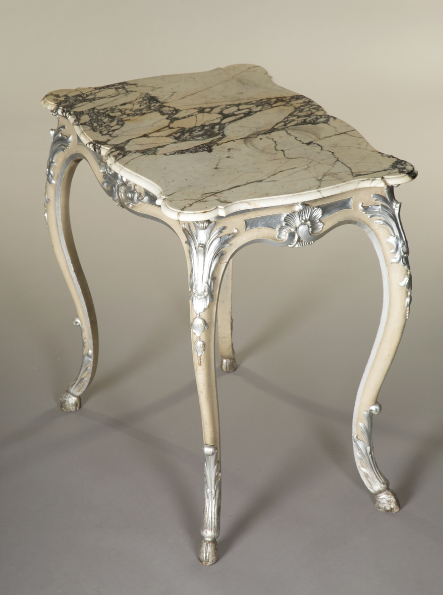 Rektangulært bord med treunderstell og marmorplate i nyrokokko. Malt lysegrått med forsølvete ornamenter. Sort og hvit marmorplate med svunget kontur. Cabrioleben med kloveavslutning. Sargens midtfelter har på kortsidene utskåret rocaille, og på langsidene skåret rankeverk. Bena har også skåret rankeverk.
