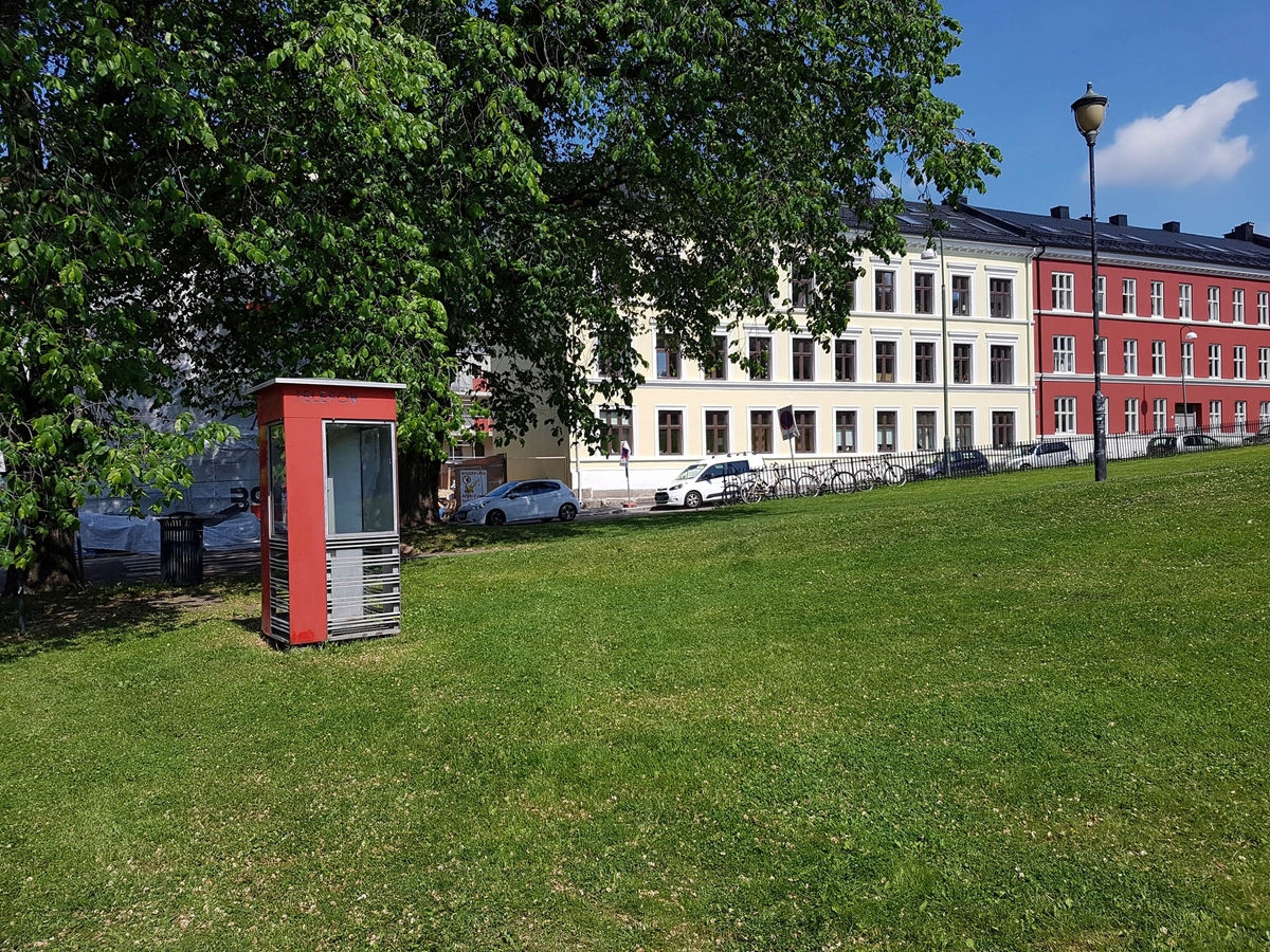 This is the story of how Norway’s most important conversation-space was designed by a young, freshly graduated man from Bergen.

“Norwegian architects are hereby invited…”
In the autumn of 1932, Oslo Telefonanlegginitiated an architectural competition. Finally, Oslo would get its own telephone booth. The city had had so called “talking-stations” from 1885, which in turn were overtaken by automatic telephones 
 only available at selected Narvesen kiosks. The state 
was of the opinion that now was the time to offer the public a better service; public telephone booths open 24/7, like the ones they already had in Sweden and England. But what would they look like, these new telephone booths? What considerations would it
 be necessary to take when designing it? The telegraph board developed a detailed list of demands and restraints: “The booth is intended to be placed outside on the streets and squares and need to be designed so that snow and ice does not hinder the opening and closing of the doors,” they wrote. “To prevent vandalism, theft, uncleanliness etc. inside the booth, it needs to be designed so that from all angles one may see what is going on in there.” Additionally, it would need to withstand storms and bad weather, and “preferably also being whipped by rain mixed with seawater” 

This was not all: The appearance would have to be «pleasing». The booth also needed to be movable, so that it could be taken in to be serviced at Telegrafverket’s main workshops. The reqired material was iron, and the surface was to be spray painted  preferably using car-body paint. There was a requirement for “a writing shelf, a pack shelf, and a suitable place for the telephone catalogue.” Also, there would need to be an illuminated TELEFON  sign, easily visible from all four angles. The total cost for each booth should not exceed 1000 kroner. The first prize for coming up with such a product was 800 kroner.

“Norwegianarchitects are hereby invited to partake in a competition for the design of a telephone booth…”  

The man with the solution
«At some point in 1932, Georg Fredrik sat at a party in Bergen. Maybe he felt a bit lost and forgotten as he often had throughout his life. He retreated to a quiet corner, took out a pencil and strted doodling on a matchbox.  According to my mother, this was how the telephone booth came into being.” In the book “Norges lille røde  historien om telefonkiosken,” Lars Fasting describes his father, the man who is far less known than the iconic architctural structure he left behind. Georg Fredrik Fasting was from Bergen, born into a family of working people and smallholders. One unusual facet of Georg Fredrik was that he was born without ears. His mother made sure he learnt to speak, read and write, 
ut Lars Fasting indicates that his father would seek refuge in drawing when the social challenges became too much to bear. And in the end drawing became his profession. In 1924 he secured a guarantor for a student loan, and started studying to become an a
rchitect at the NTH. Throughout the 1930s he entered several architectural competitions, with drafts produced, according to his son, “after work and in the late hours of the night.”

His efforts were not wasted. Out of 93 entries, with names such as “Flirt”, “Brrr”, “Ring” and “Amor”, the jury selected Fasting’s submission, “RIKS” as the new telephone booth: “The draft shows a strikingly simple solution to the task, technically as well as aesthetically well worked out.”

Taut and provident
Simple and aesthetc are the keywords here. Fasting had designed a booth pointing towards the future, and to modernism. Just how modern it was can be seen by comparing RIKS to the British telephone booth, also designed in the interwar-era. While the British version with it classicistic style is looking back to the heyday of the empire, Fasting’s booth is progressive and functionalistic. Like most Norwegian architects, Fasting broke with the classicistic style of architecture after the Stockholm-exhibition in 1930. “After it, almost all buildings erected in Norway until the German invasion in 1940, were in the functionalistic architectural style,” writes senior curator of architecture at the Norwegian National Museum, Ulf Grønvold, in the book, “Den lille røde”.“TheNorwegian booth is a piece of functionalistic architecture, an asymmetric composition with its roof slab overhanging the word TELEFON, in bold sans seraph lettering,”concludes Ulf Grønvold.

Fashionably red
And it was red. Fasting chose a colour which was part of the modern palette. “A bright red colour, but not as shiny as a signal red, the character of the colour places it among the fashionable colours within functionalism,” states paintings conservator and researcher in NIKU (Norwegian Institute for Cultural Heitage Research), Jon Brænne. In his opinion, Fasting went for visibility without making the booth stand out too much from its surroundings. The original colour was in use up to around 1950, when it changed to signal red. Towards the end of the 1970s the clour was again adjusted towards today’s orangey red.

The design, however, has not changed. RIKS is eighty years and still looks remarkably good. That’s what makes Fasting’s telephone booth a classic  even before it was added to DOCOMOMO’s list over moden icons of design. For Telenor, the telephone booth has served as a pathway into the hearts of the public. For many, Telenor (Televerket) was synonymous with exactly this telephone booth, because this was where one would go to place a call. Having a home
phone was not common until the 1980s. As such the red box became part of the Norwegian everyday and consciousness. The symbol- and publicity value of this is hard to evaluate, but in 2007 it was time to give honour where honour was due, Telenor, in consul
tation with the Directorate for Cultural Heritage, decided to preserve 100 telephone booths for all eternity.

And what about Georg Fredrik Fasting? What happened to him? At the age of 56 an entry in his diary states: «I CAN HEAR». As the first person in th world he had undergone an operation where he had ear canals constructed and eardrums fitted. For the rest of his life, the man behind Norway’s own telephone booth could answer the telephone himself.

Source: Norges lille røde historien om telefonkiosken (2007), issued by The Norwegian Telecom Museum and Telenor Cultural Heritage.