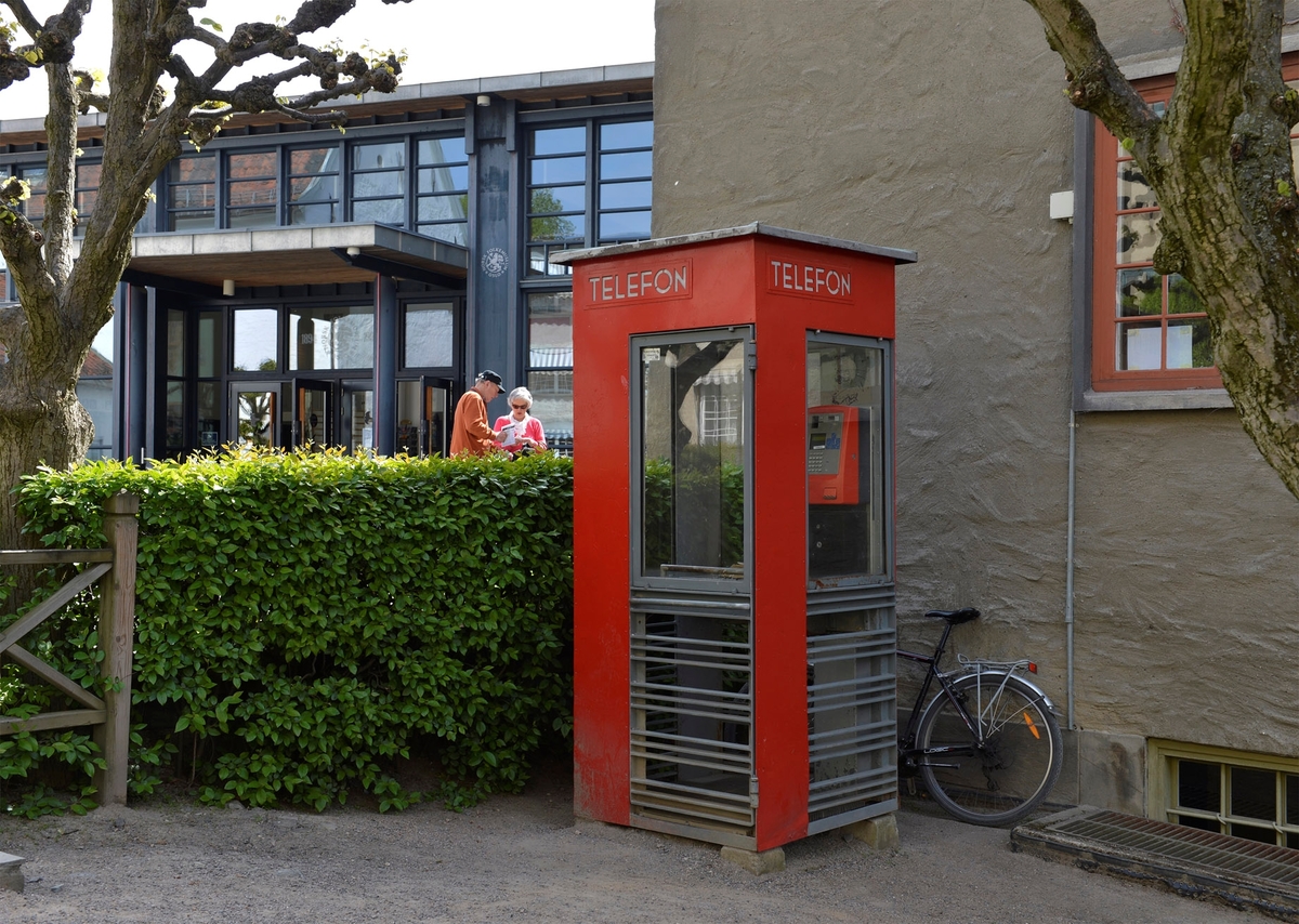 This is the story of how Norway’s most important conversation-space was designed by a young, freshly graduated man from Bergen.

“Norwegian architects are hereby invited…”
In the autumn of 1932, Oslo Telefonanlegginitiated an architectural competition. Finally, Oslo would get its own telephone booth. The city had had so called “talking-stations” from 1885, which in turn were overtaken by automatic telephones 
 only available at selected Narvesen kiosks. The state 
was of the opinion that now was the time to offer the public a better service; public telephone booths open 24/7, like the ones they already had in Sweden and England. But what would they look like, these new telephone booths? What considerations would it
 be necessary to take when designing it? The telegraph board developed a detailed list of demands and restraints: “The booth is intended to be placed outside on the streets and squares and need to be designed so that snow and ice does not hinder the opening and closing of the doors,” they wrote. “To prevent vandalism, theft, uncleanliness etc. inside the booth, it needs to be designed so that from all angles one may see what is going on in there.” Additionally, it would need to withstand storms and bad weather, and “preferably also being whipped by rain mixed with seawater” 

This was not all: The appearance would have to be «pleasing». The booth also needed to be movable, so that it could be taken in to be serviced at Telegrafverket’s main workshops. The reqired material was iron, and the surface was to be spray painted  preferably using car-body paint. There was a requirement for “a writing shelf, a pack shelf, and a suitable place for the telephone catalogue.” Also, there would need to be an illuminated TELEFON  sign, easily visible from all four angles. The total cost for each booth should not exceed 1000 kroner. The first prize for coming up with such a product was 800 kroner.

“Norwegianarchitects are hereby invited to partake in a competition for the design of a telephone booth…”  

The man with the solution
«At some point in 1932, Georg Fredrik sat at a party in Bergen. Maybe he felt a bit lost and forgotten as he often had throughout his life. He retreated to a quiet corner, took out a pencil and strted doodling on a matchbox.  According to my mother, this was how the telephone booth came into being.” In the book “Norges lille røde  historien om telefonkiosken,” Lars Fasting describes his father, the man who is far less known than the iconic architctural structure he left behind. Georg Fredrik Fasting was from Bergen, born into a family of working people and smallholders. One unusual facet of Georg Fredrik was that he was born without ears. His mother made sure he learnt to speak, read and write, 
ut Lars Fasting indicates that his father would seek refuge in drawing when the social challenges became too much to bear. And in the end drawing became his profession. In 1924 he secured a guarantor for a student loan, and started studying to become an a
rchitect at the NTH. Throughout the 1930s he entered several architectural competitions, with drafts produced, according to his son, “after work and in the late hours of the night.”

His efforts were not wasted. Out of 93 entries, with names such as “Flirt”, “Brrr”, “Ring” and “Amor”, the jury selected Fasting’s submission, “RIKS” as the new telephone booth: “The draft shows a strikingly simple solution to the task, technically as well as aesthetically well worked out.”

Taut and provident
Simple and aesthetc are the keywords here. Fasting had designed a booth pointing towards the future, and to modernism. Just how modern it was can be seen by comparing RIKS to the British telephone booth, also designed in the interwar-era. While the British version with it classicistic style is looking back to the heyday of the empire, Fasting’s booth is progressive and functionalistic. Like most Norwegian architects, Fasting broke with the classicistic style of architecture after the Stockholm-exhibition in 1930. “After it, almost all buildings erected in Norway until the German invasion in 1940, were in the functionalistic architectural style,” writes senior curator of architecture at the Norwegian National Museum, Ulf Grønvold, in the book, “Den lille røde”.“TheNorwegian booth is a piece of functionalistic architecture, an asymmetric composition with its roof slab overhanging the word TELEFON, in bold sans seraph lettering,”concludes Ulf Grønvold.

Fashionably red
And it was red. Fasting chose a colour which was part of the modern palette. “A bright red colour, but not as shiny as a signal red, the character of the colour places it among the fashionable colours within functionalism,” states paintings conservator and researcher in NIKU (Norwegian Institute for Cultural Heitage Research), Jon Brænne. In his opinion, Fasting went for visibility without making the booth stand out too much from its surroundings. The original colour was in use up to around 1950, when it changed to signal red. Towards the end of the 1970s the clour was again adjusted towards today’s orangey red.

The design, however, has not changed. RIKS is eighty years and still looks remarkably good. That’s what makes Fasting’s telephone booth a classic  even before it was added to DOCOMOMO’s list over moden icons of design. For Telenor, the telephone booth has served as a pathway into the hearts of the public. For many, Telenor (Televerket) was synonymous with exactly this telephone booth, because this was where one would go to place a call. Having a home
phone was not common until the 1980s. As such the red box became part of the Norwegian everyday and consciousness. The symbol- and publicity value of this is hard to evaluate, but in 2007 it was time to give honour where honour was due, Telenor, in consul
tation with the Directorate for Cultural Heritage, decided to preserve 100 telephone booths for all eternity.

And what about Georg Fredrik Fasting? What happened to him? At the age of 56 an entry in his diary states: «I CAN HEAR». As the first person in th world he had undergone an operation where he had ear canals constructed and eardrums fitted. For the rest of his life, the man behind Norway’s own telephone booth could answer the telephone himself.

Source: Norges lille røde historien om telefonkiosken (2007), issued by The Norwegian Telecom Museum and Telenor Cultural Heritage.
